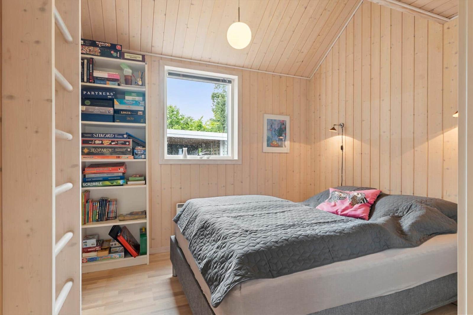 Schlafzimmer mit Holzwand, Bett, Fenster und Bücherregal.