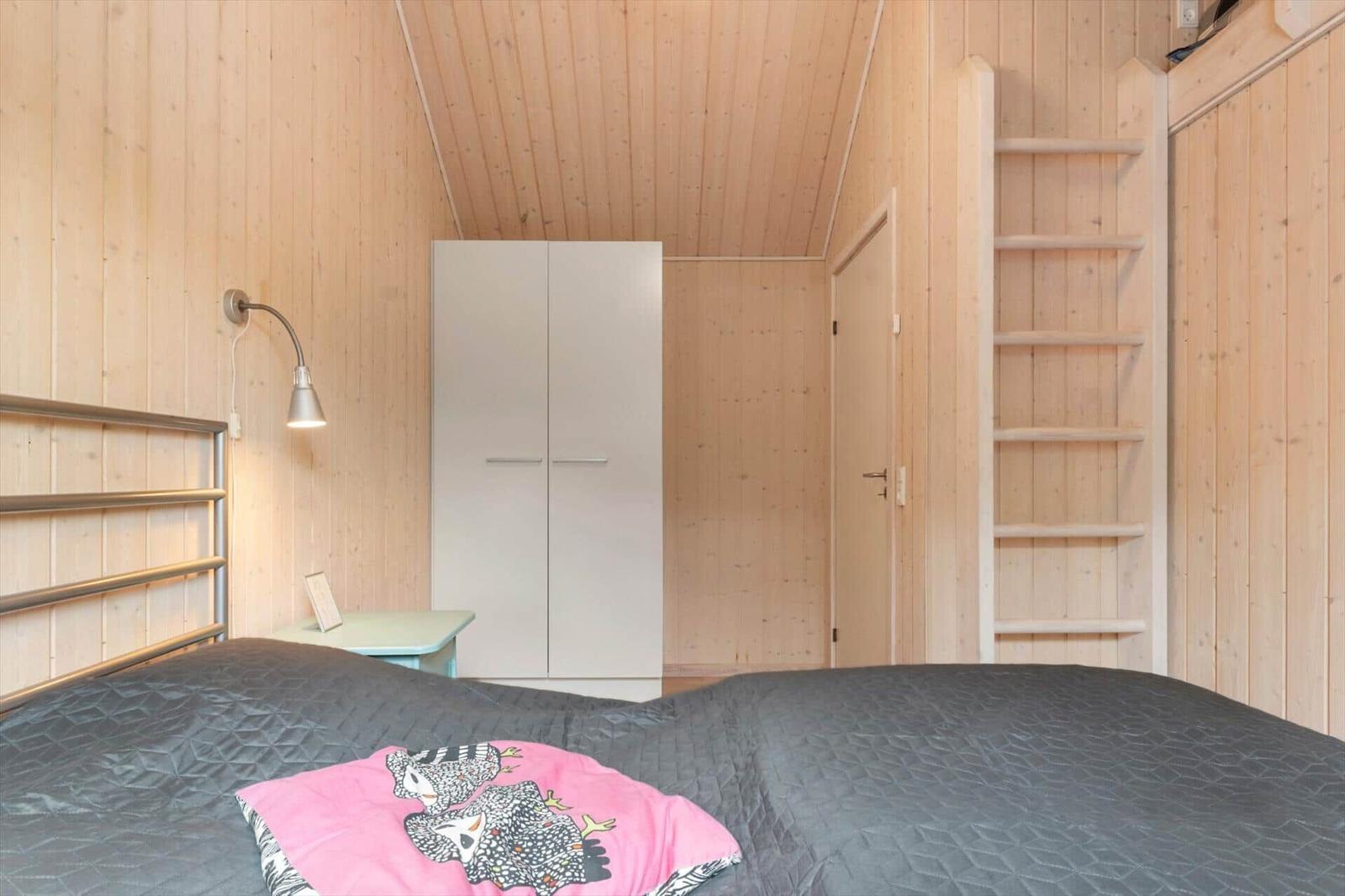 Schlafzimmer mit Holzwand, Bett, Kleiderschrank und Leiter.