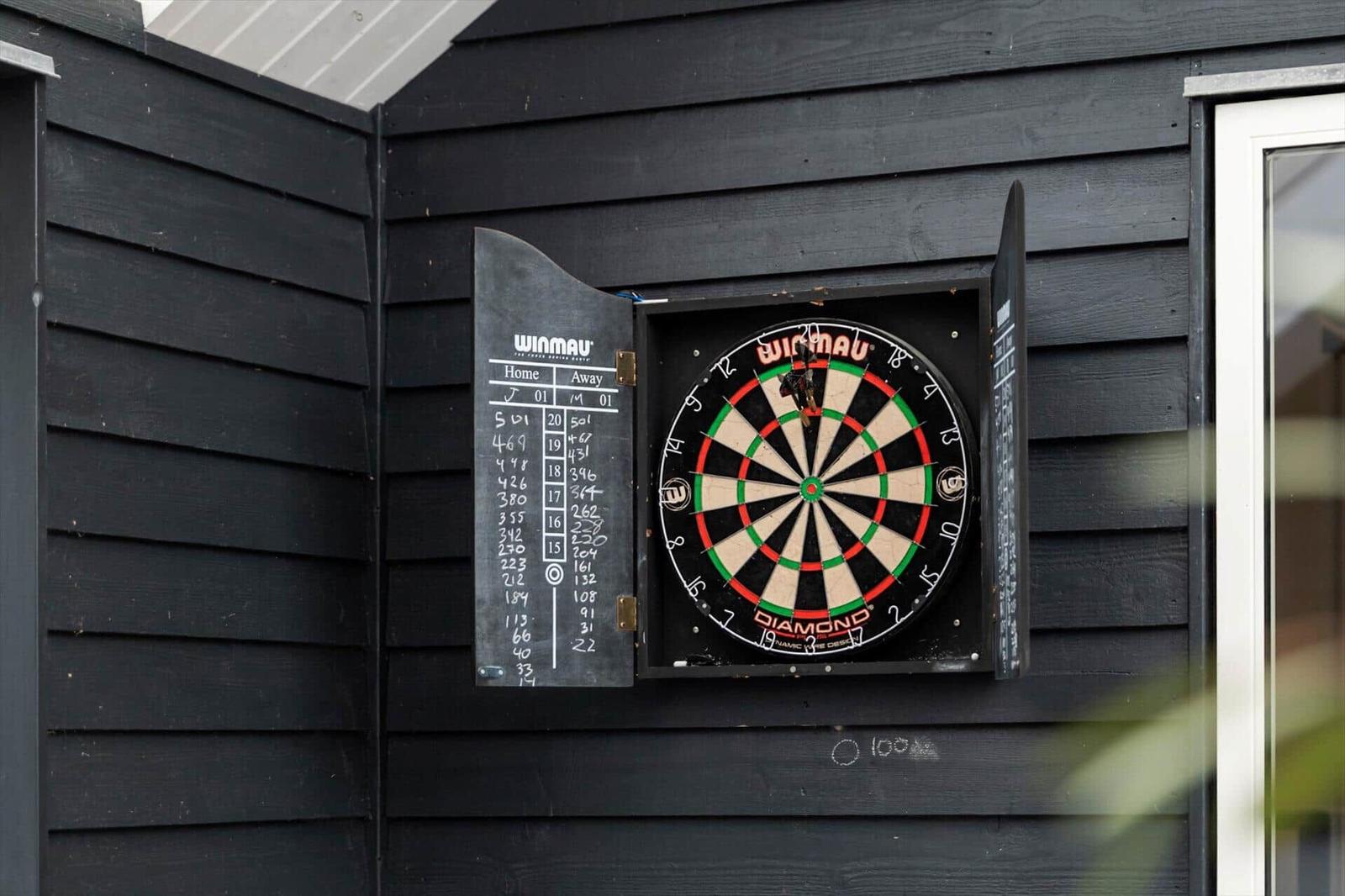 Dartboard mit Tafel an schwarzer Holzwand montiert.
