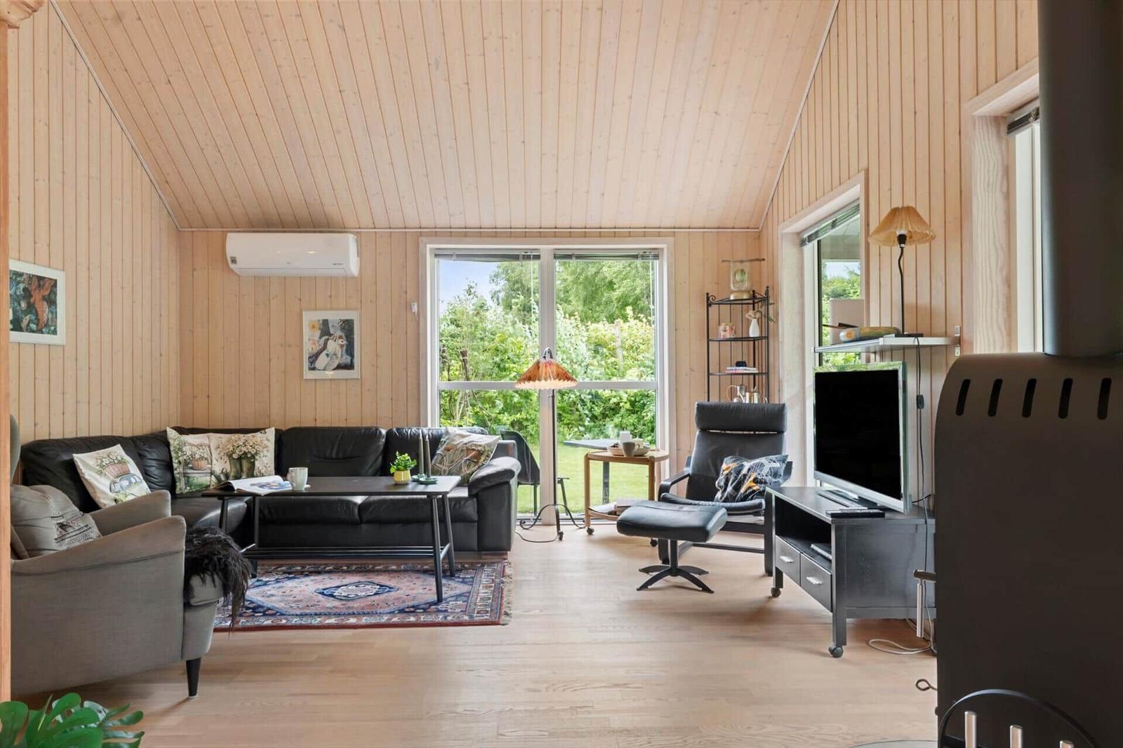 Wohnzimmer mit Sofa, Sessel und Fernseher. Holzwände und große Fenster.