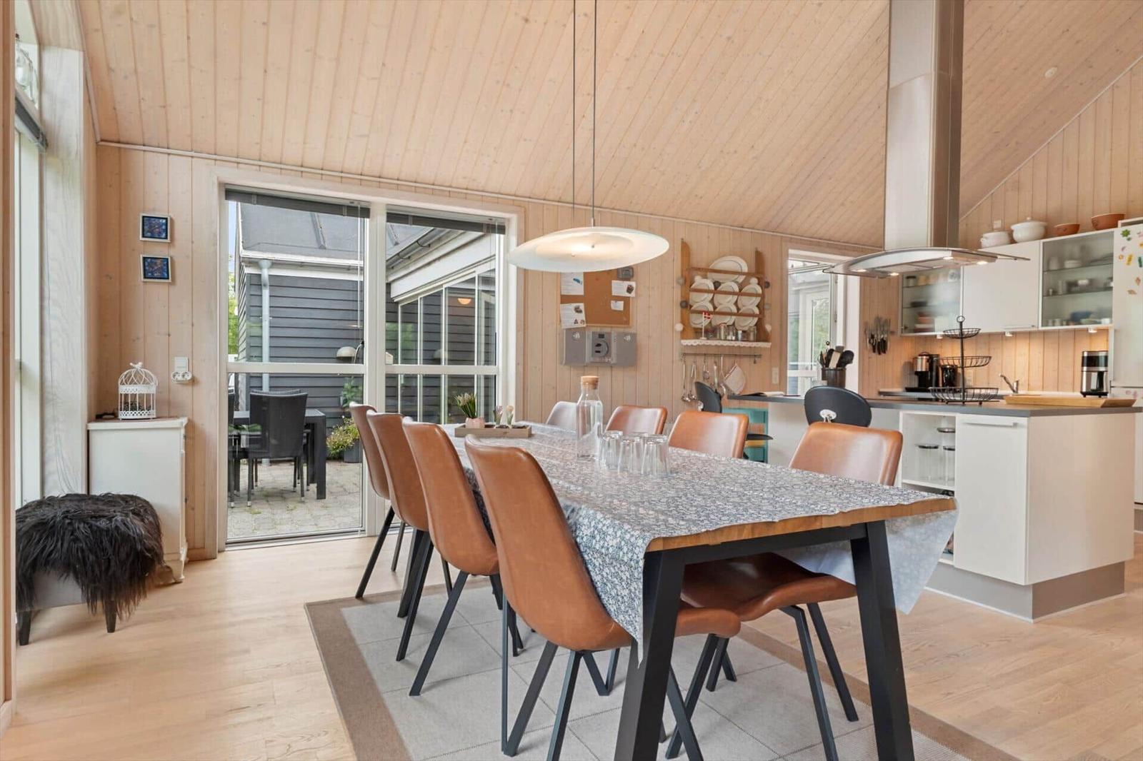 Essbereich mit Holzdecke und Küchenzeile. Tisch mit braunen Stühlen und Glas.