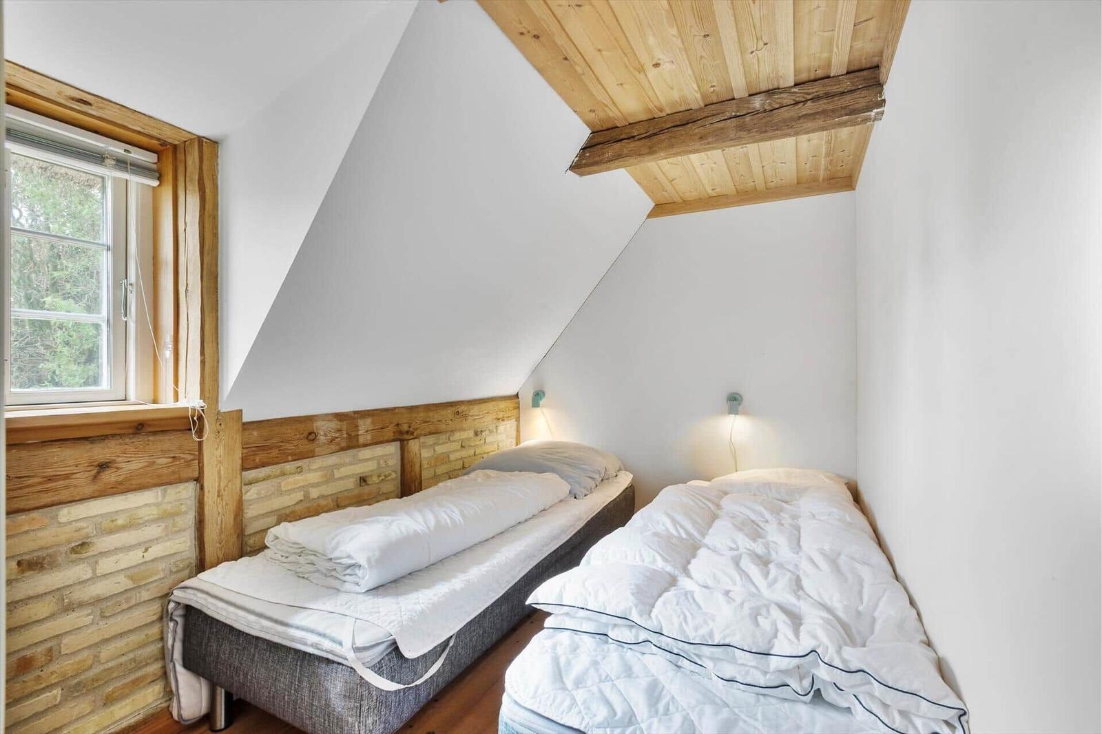 Zwei Betten in einem Dachzimmer mit Holzdecke und Fenster.