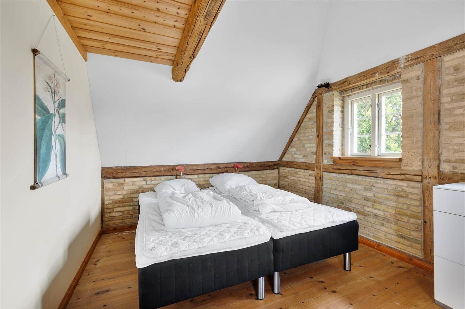Zimmer mit Doppelbett, Holzdecke und Fenster. Wandgestaltung mit Stein und Holz.