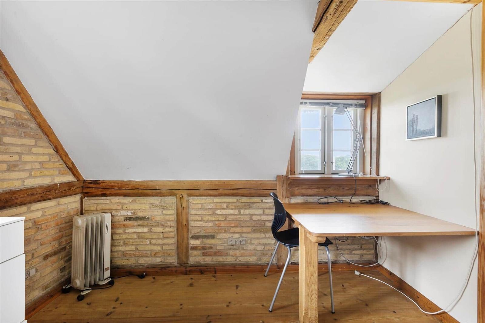 Schlafzimmer mit Holztisch, Stuhl und Fenster. Wand aus Ziegel und Holz.