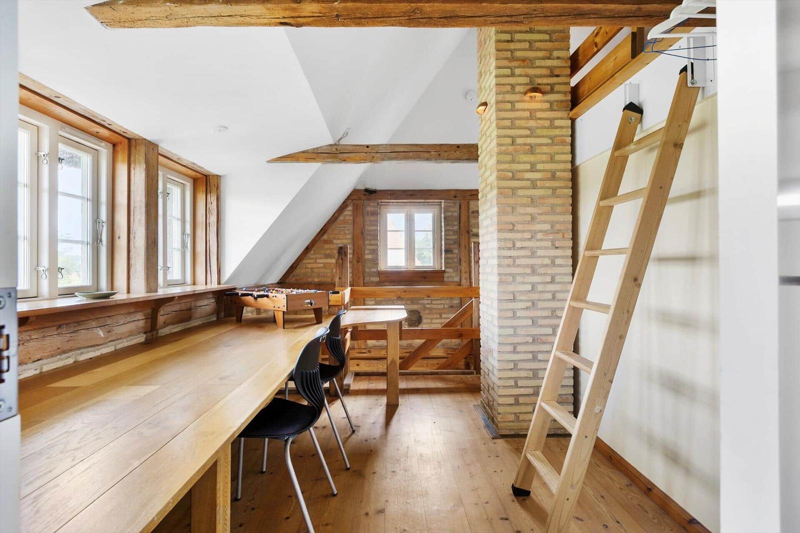 Raum mit Holztisch, Stühlen, Tischfußball und Leiter. Holzdielen, Fenster und Steinwand.