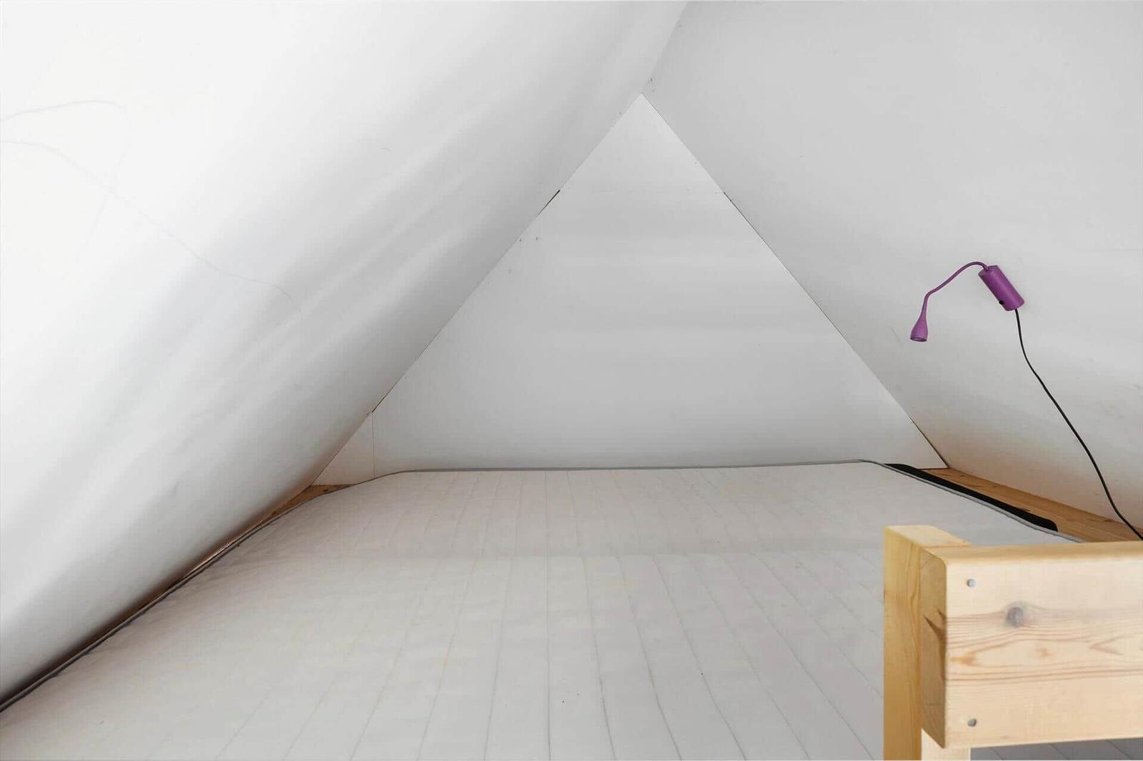 Schlafzimmer mit Dachschrägen, Holzbett und lila Wandlampe.