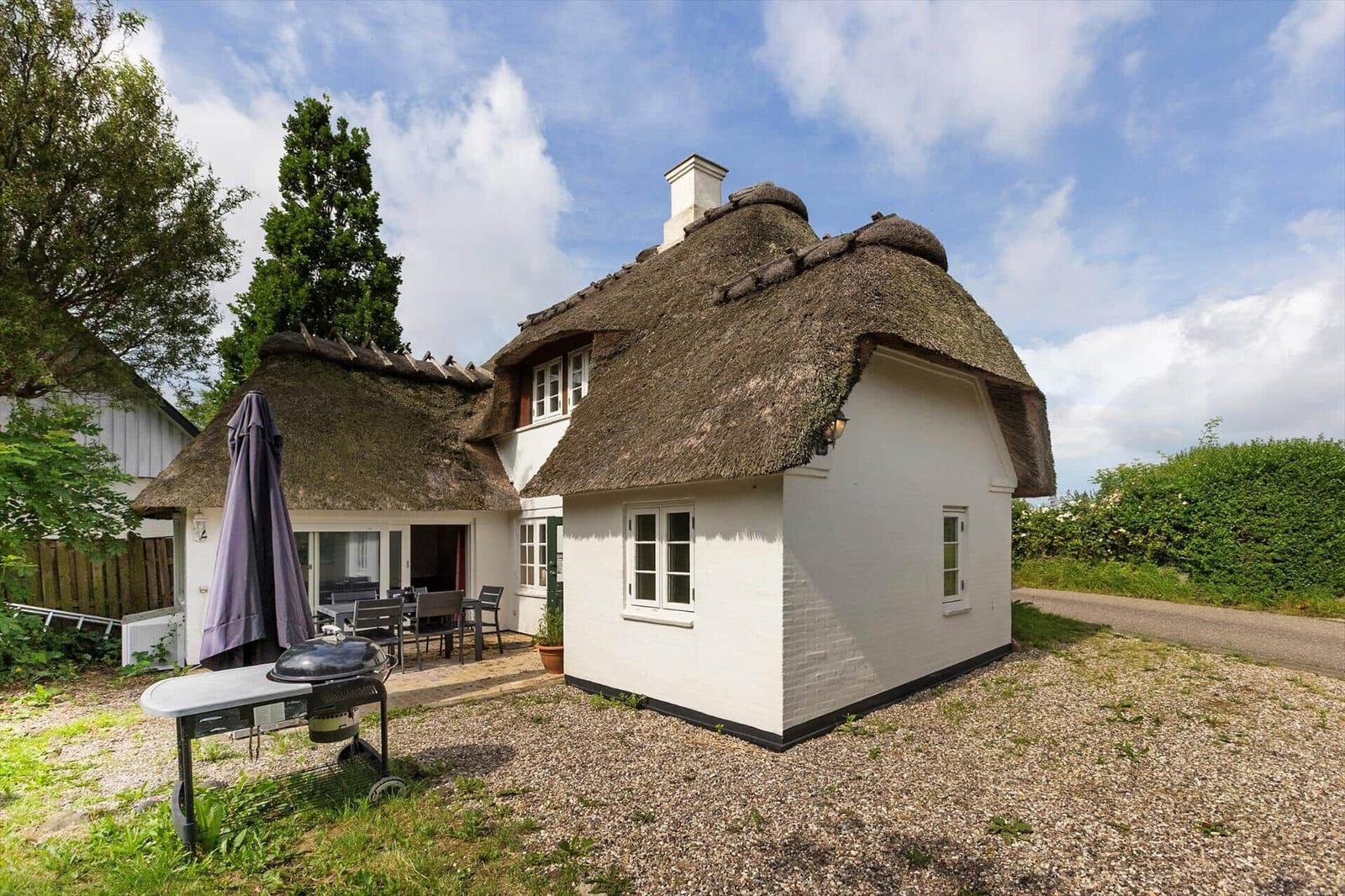 Haus mit Strohdach, Terrasse und Grillplatz im Freien.