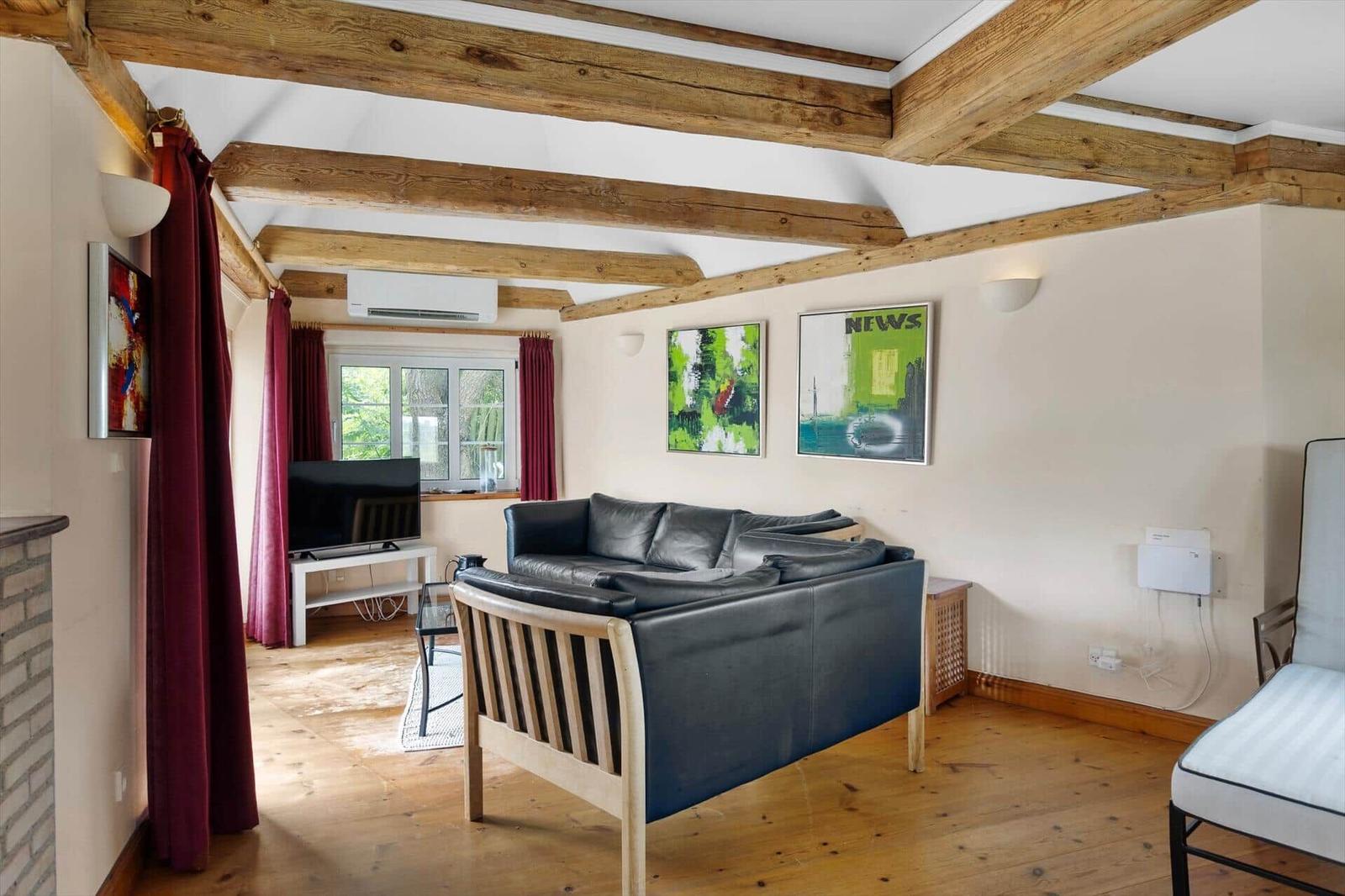 Wohnzimmer mit Holzbalken, Sofa, Fernseher und Fenster mit roten Vorhängen.