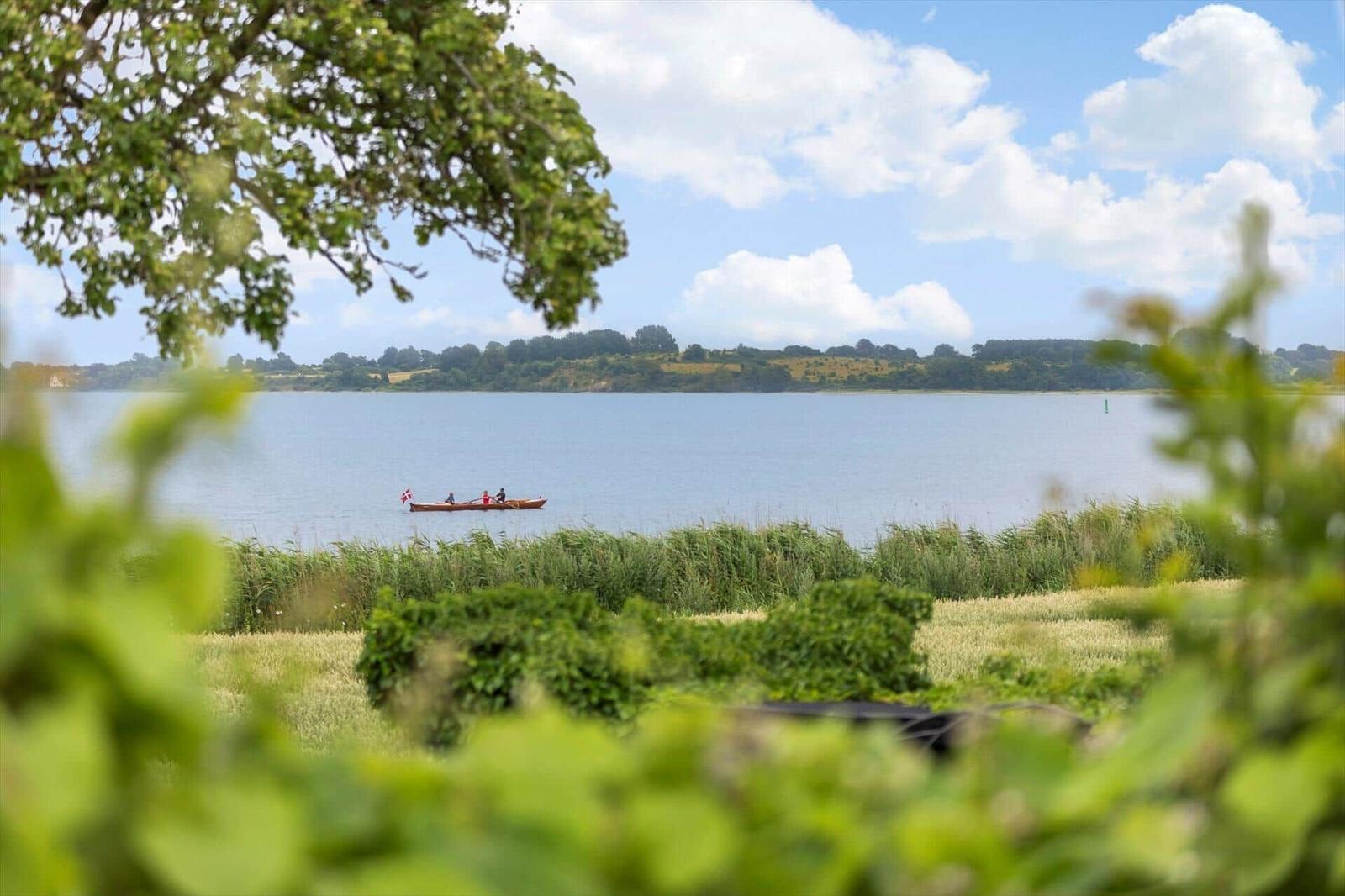 Ein kleines Boot mit drei Personen fährt auf einem See. Grüne Bäume und Wiesen umgeben den See.