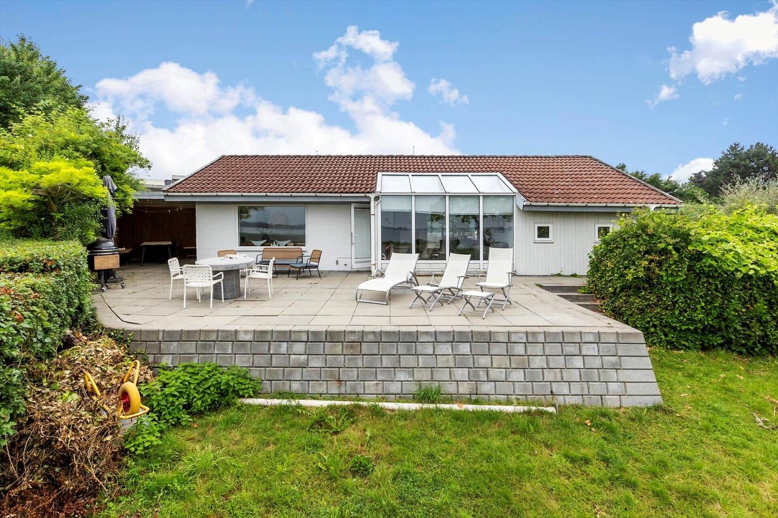 Haus mit Terrasse, Sonnenliegen und Grillplatz. Grünanlagen umgeben die Außenbereiche.