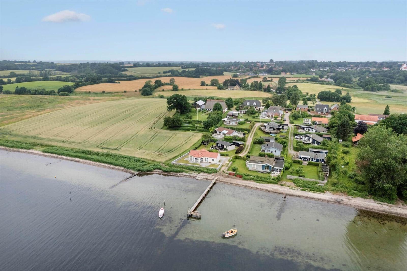 Haus am Wasser mit Bootssteg und umliegenden Feldern.