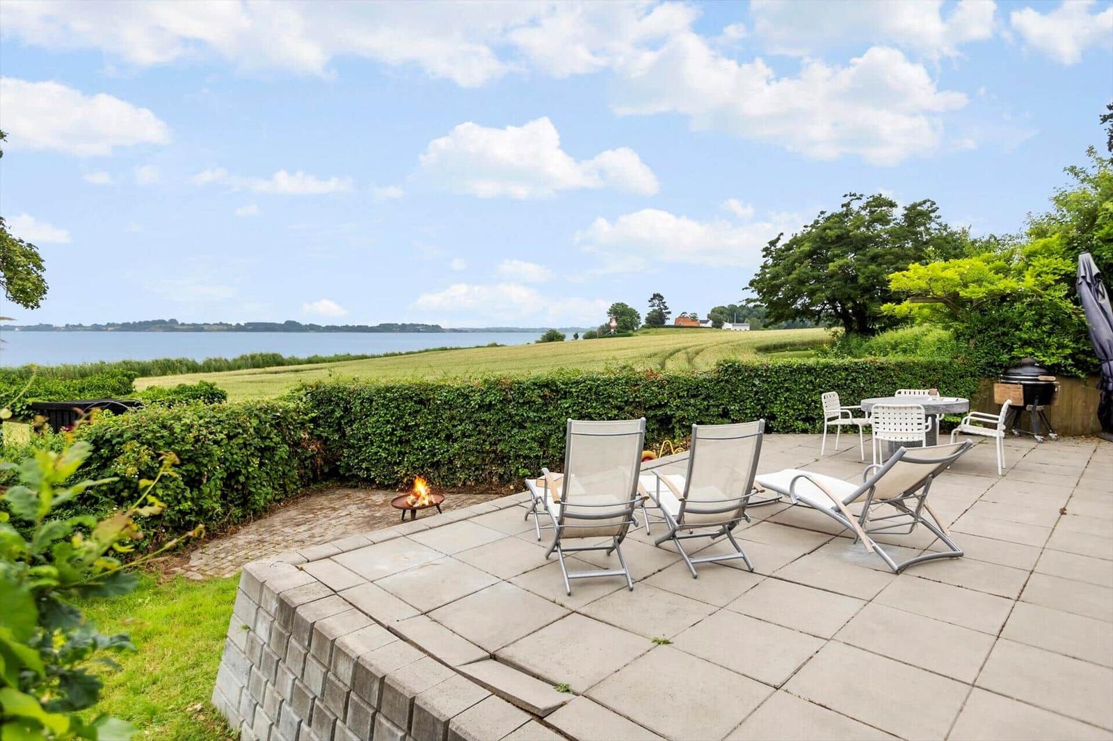 Terrasse mit Sitzgelegenheiten und Grillplatz. Blick auf Felder und Wasser.
