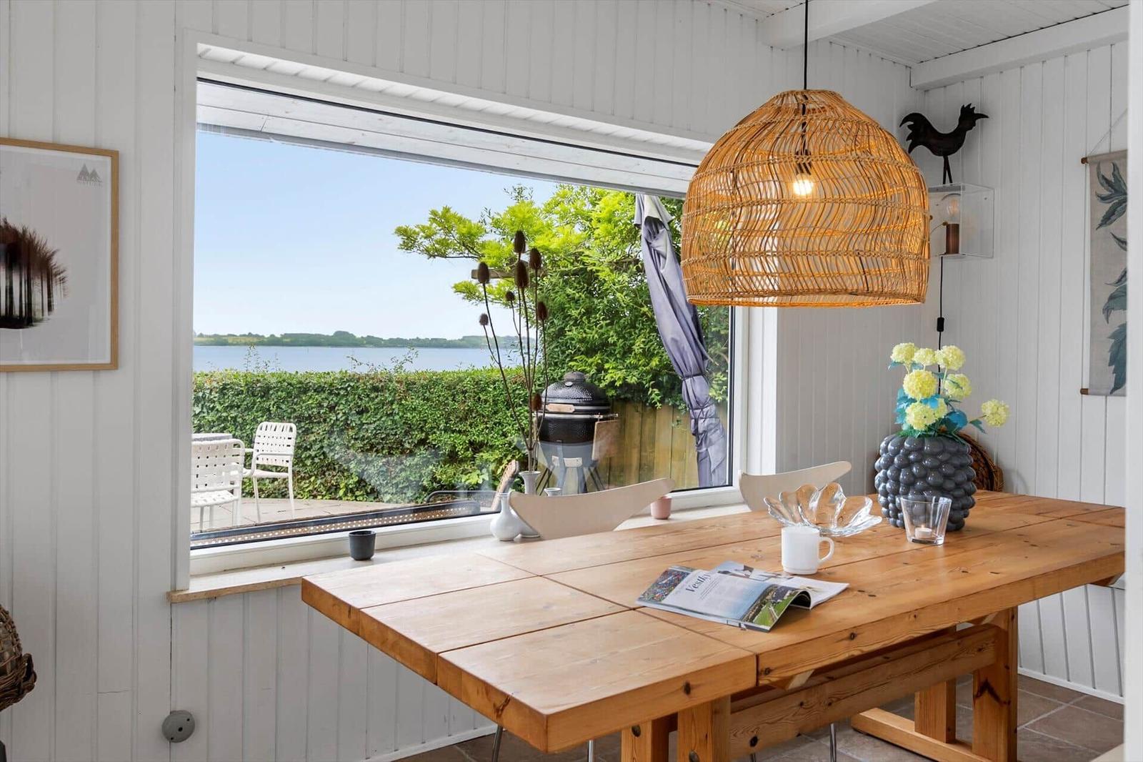 Holztisch mit Stühlen und Blick auf den Garten. Wicker-Lampe und Blumenarrangement.