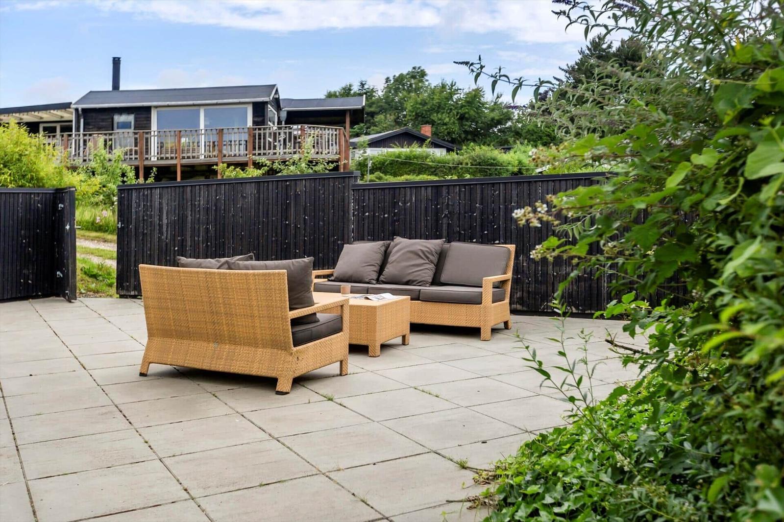 Terrasse mit Sitzgruppe, schwarzer Zaun und Gartenhaus im Hintergrund.