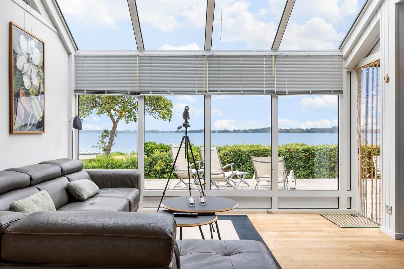 Ein Wohnbereich mit Blick auf einen See. Es gibt einen Sofa, einen Tisch und einen Teleskop.