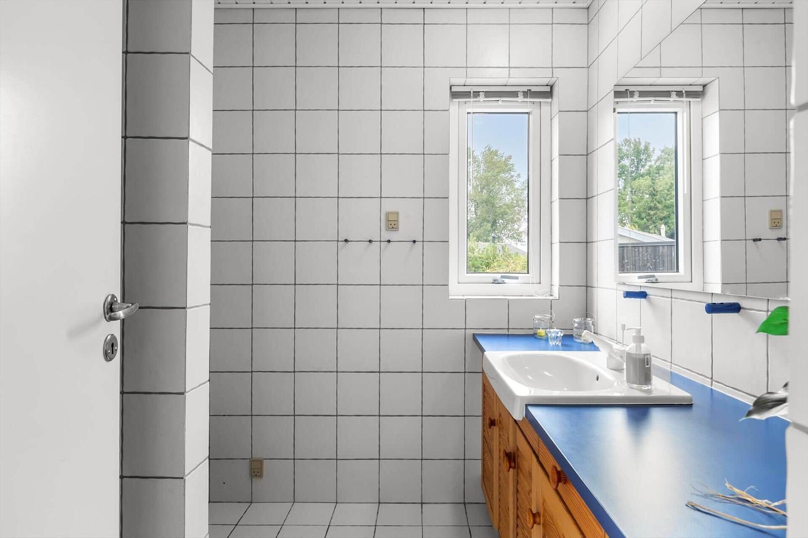Badezimmer mit weißen Fliesen, blauem Waschtisch und Fenster mit Blick auf Grün.