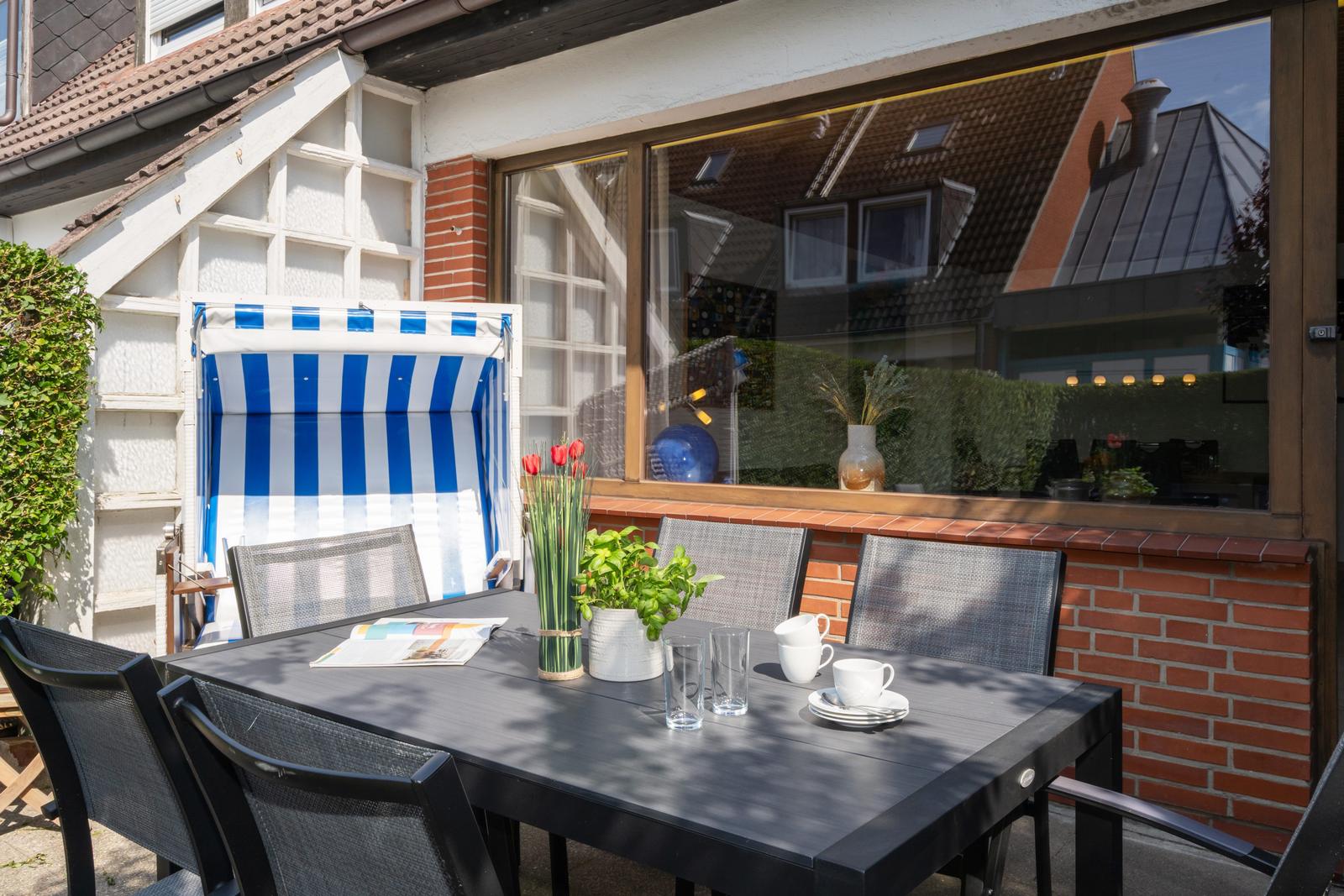 Terrasse mit Tisch, Stühlen und blau-weißem Sonnenschirm. Fenster reflektiert Nachbarhäuser.