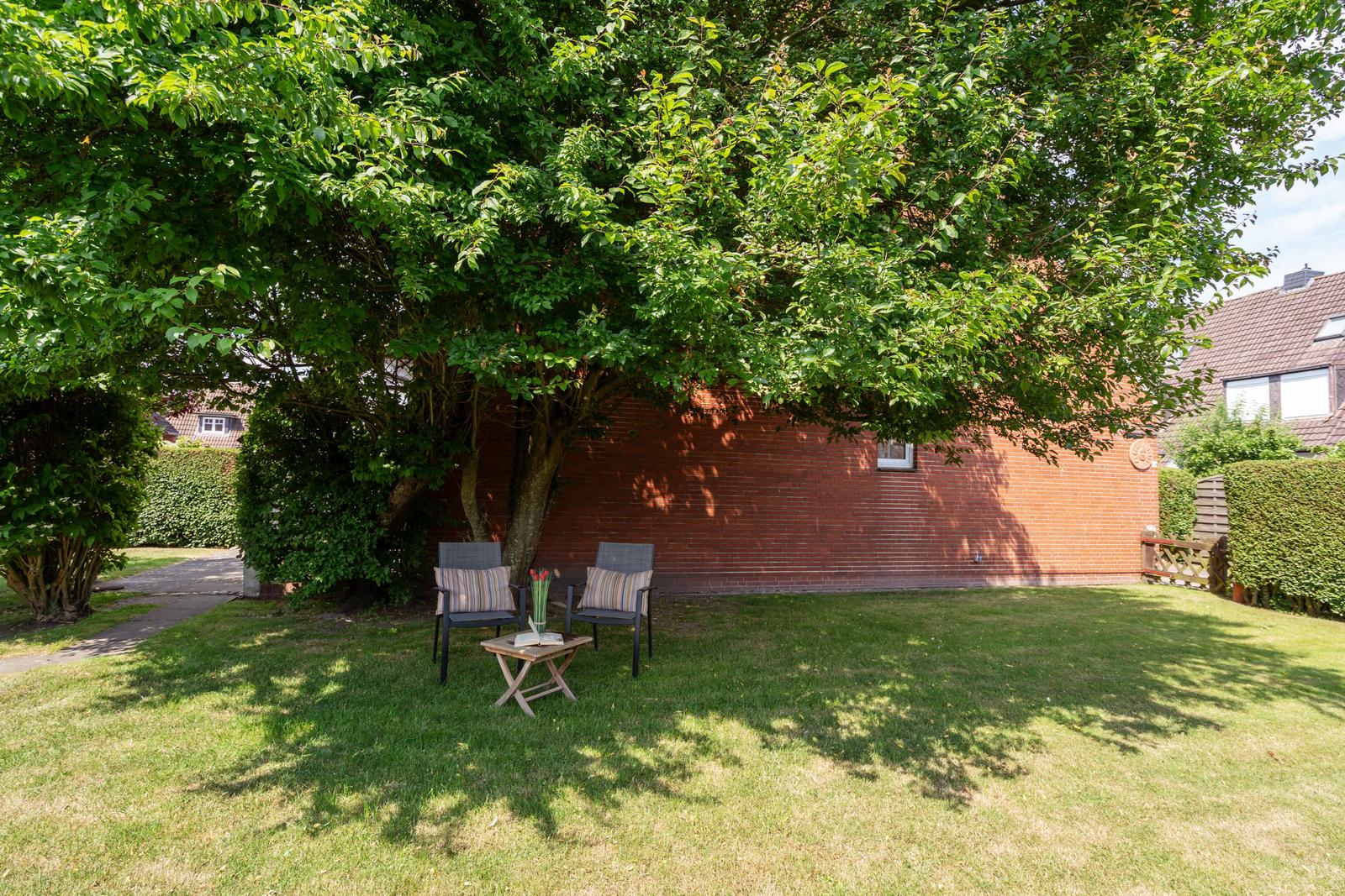 Garten mit Sitzgruppe unter Baum, Rasenfläche und Backsteinmauer im Hintergrund.