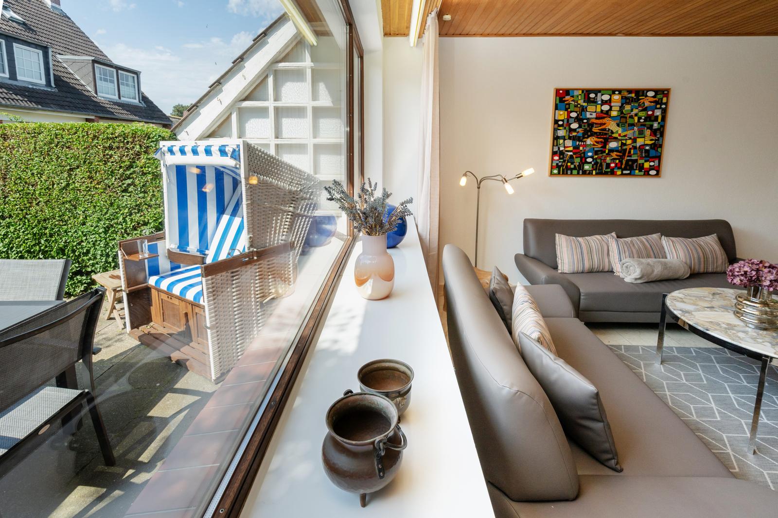 Wohnbereich mit Sofa und Fensterblick auf Terrasse mit Strandkorb.