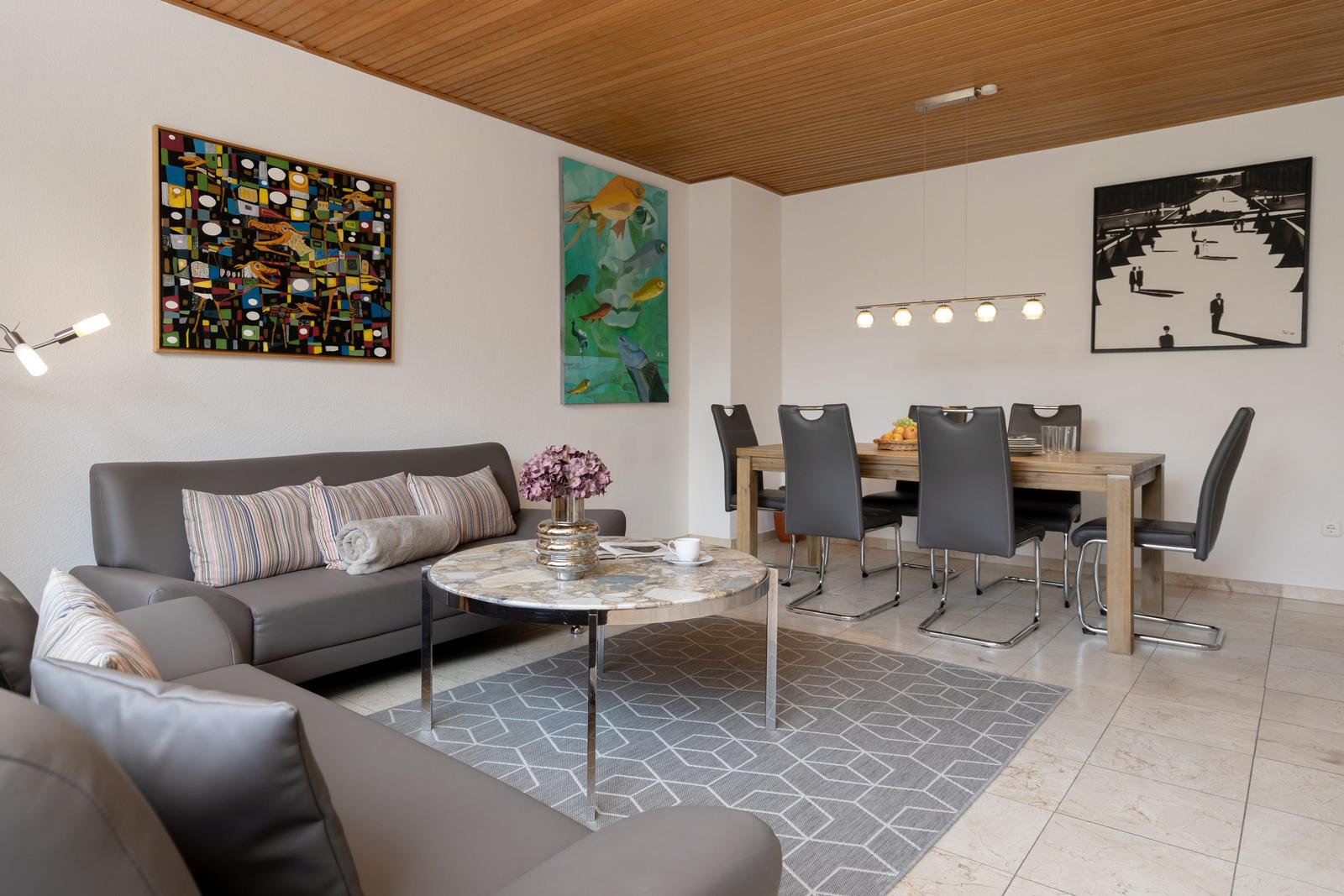 Wohn- und Essbereich mit Sofa, Tisch und Stühlen sowie Wandbildern.