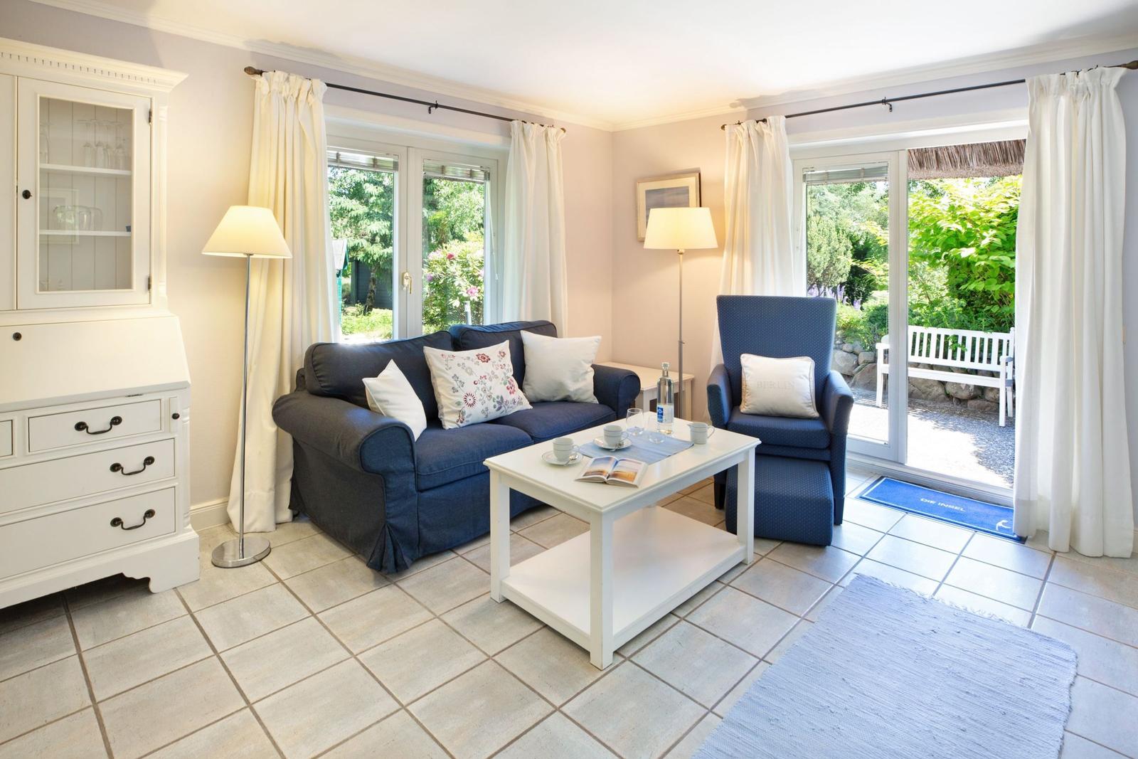 Living room with sofa, armchair, and table. Entrance to terrace with garden view.