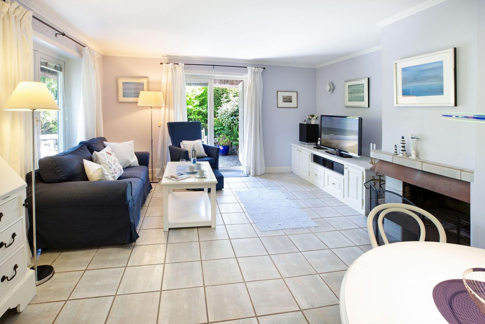 Living room with sofa, TV, and fireplace. Doorway to terrace with garden view.