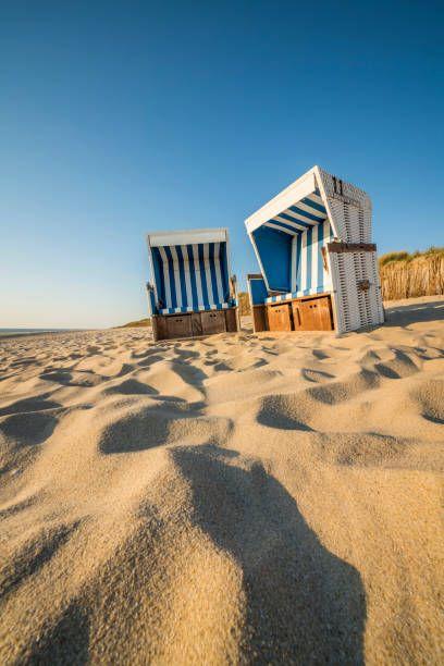 Zwei blaue Strandkörbe stehen auf Sand unter blauem Himmel.