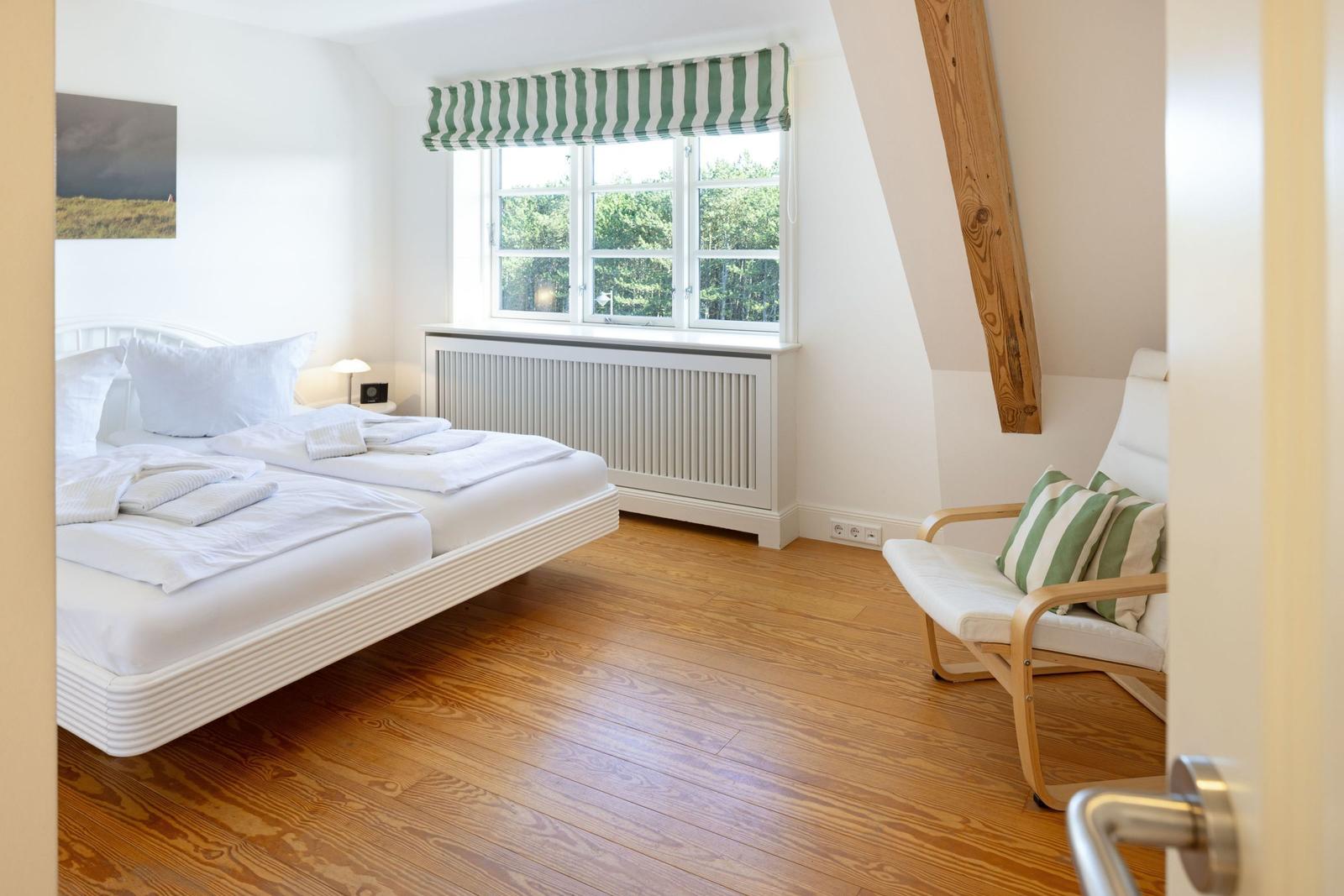 Schlafzimmer mit Doppelbett, Holzboden und grün-weißem Fensterrollo.