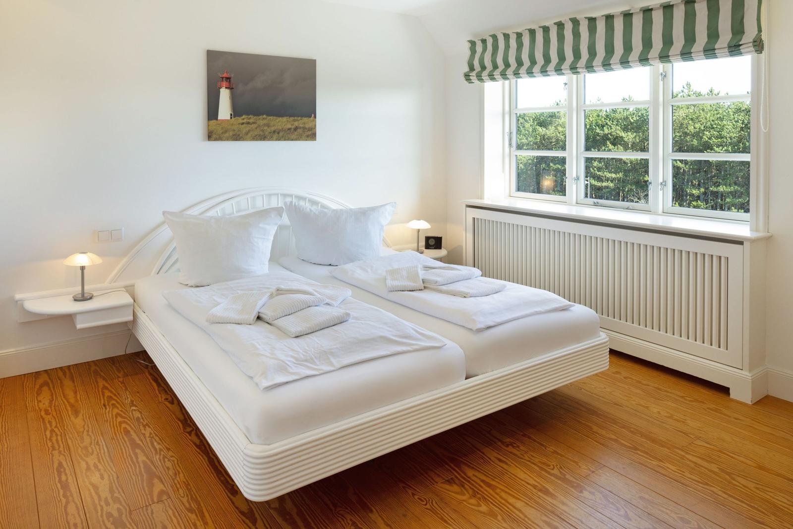 Schlafzimmer mit Doppelbett, Holzboden und Fenster mit Blick auf Bäume.