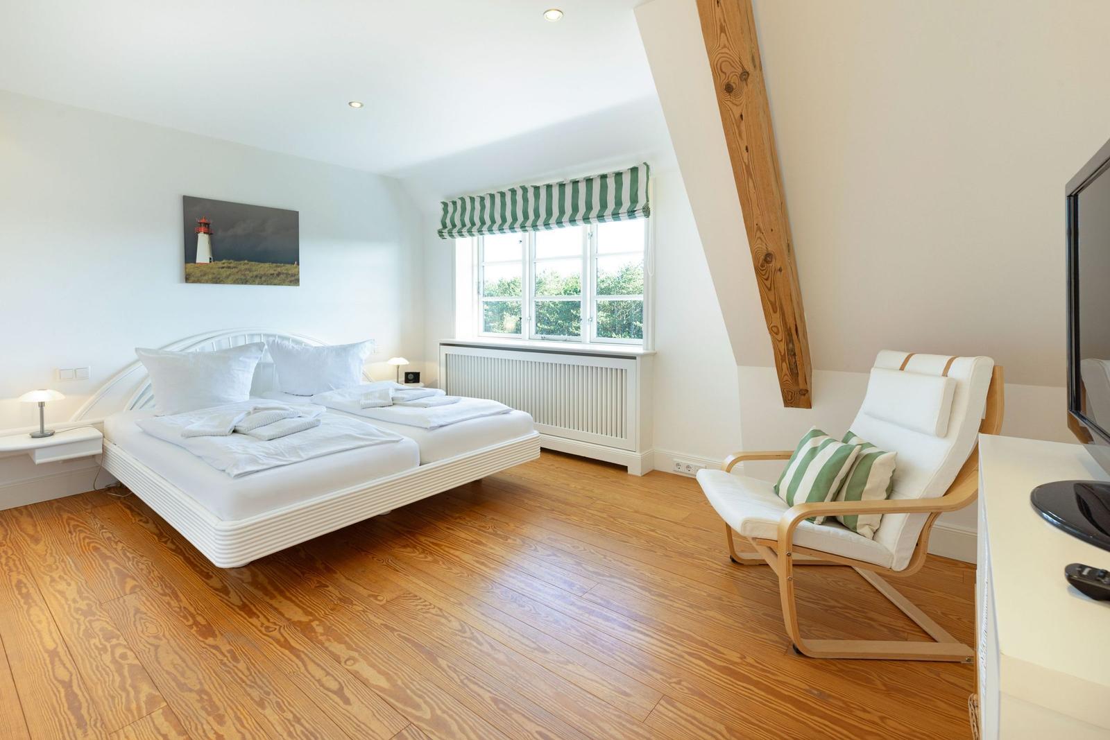 Schlafzimmer mit Doppelbett, Holzboden und Sessel. Fenster mit grün-weißem Rollladen.