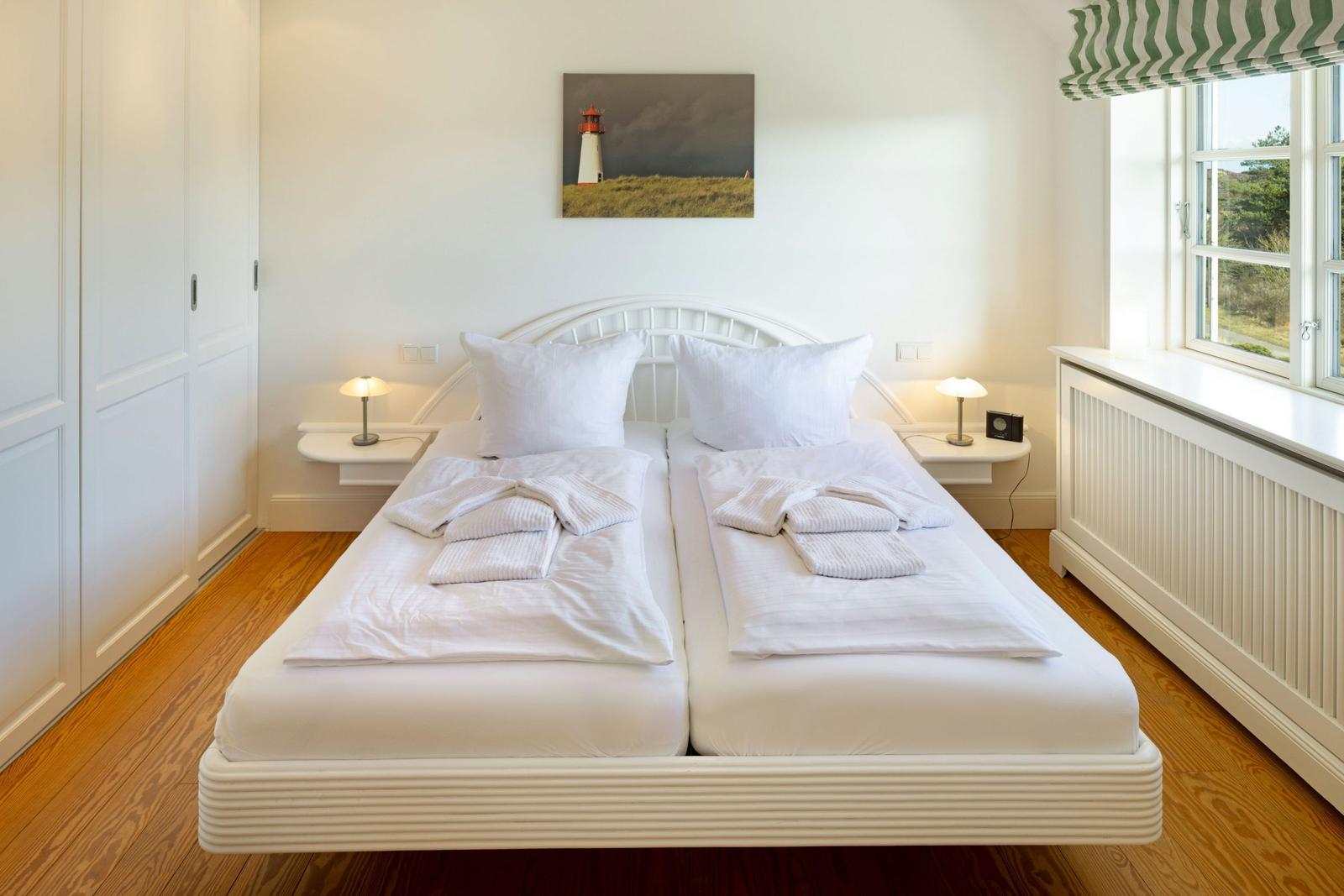 Schlafzimmer mit Doppelbett, weißen Wänden und Holzboden. Fenster mit grün-weißem Rollladen.