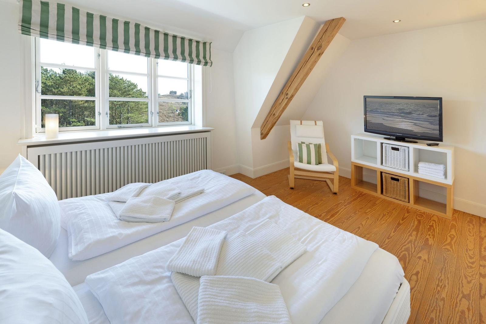 Schlafzimmer mit Dachschräge, Bett, TV und Fenster mit Blick auf Wald.