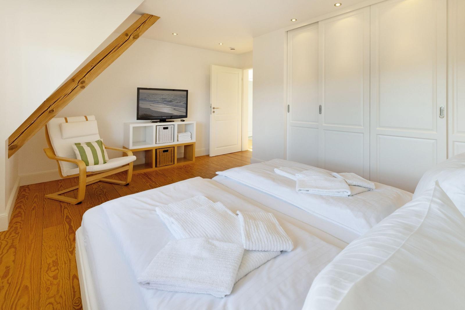 Schlafzimmer mit Doppelbett, TV und Holzfußboden unter Dachschräge.