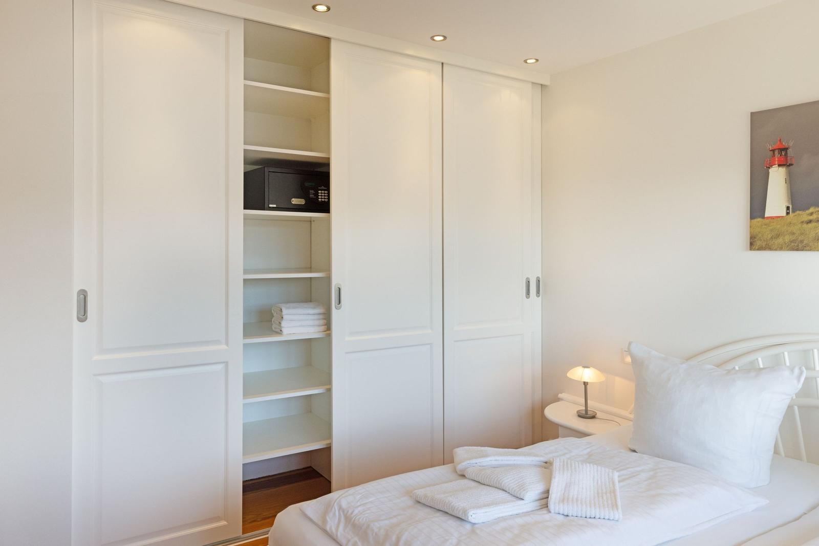 Schlafzimmer mit weißem Schrank, Bett und Nachttisch. Auf dem Bett liegen Handtücher.