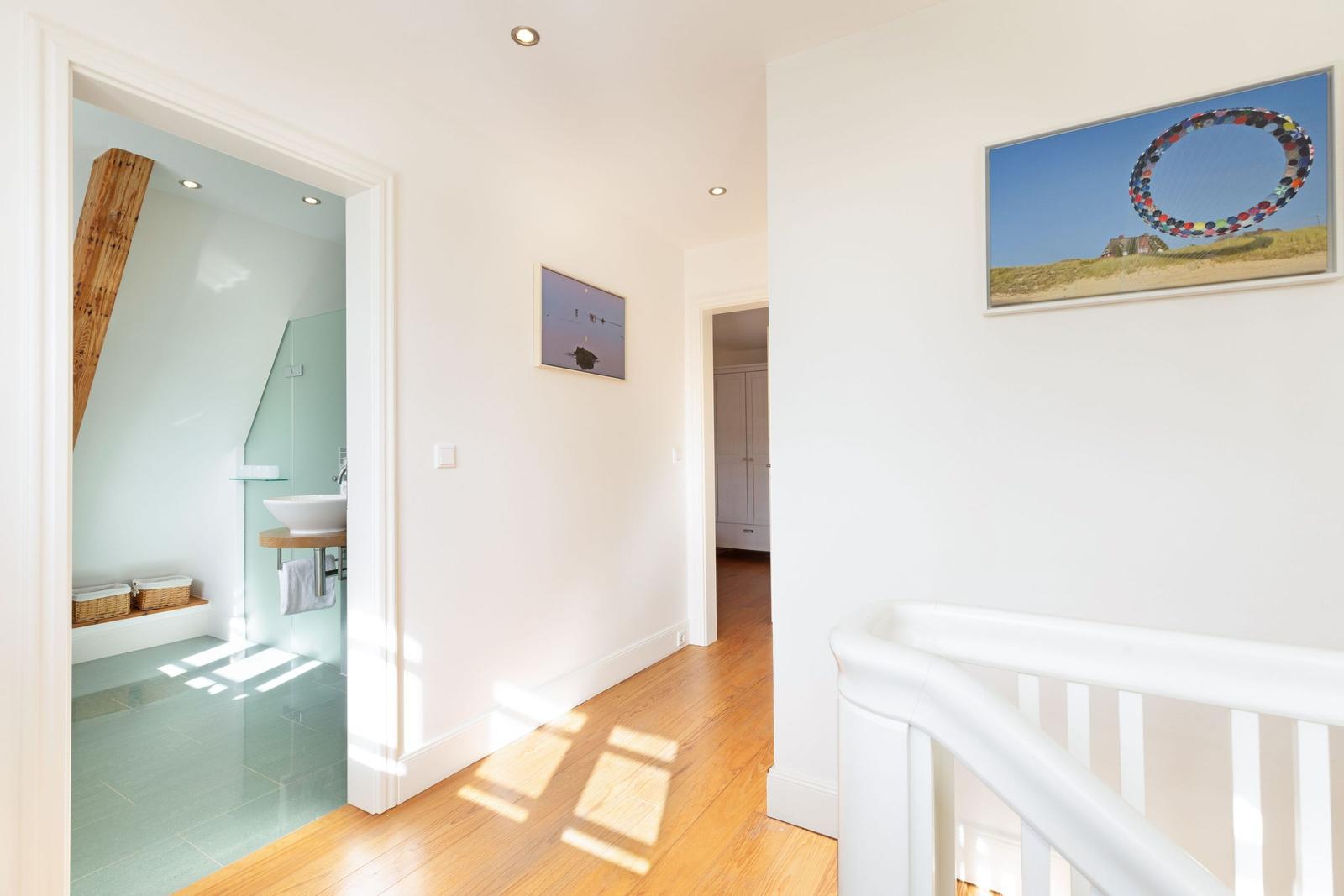 Hausflur mit Holzboden, weißen Wänden und Bildern an der Wand. Blick in die Badewanne und Schlafzimmer.