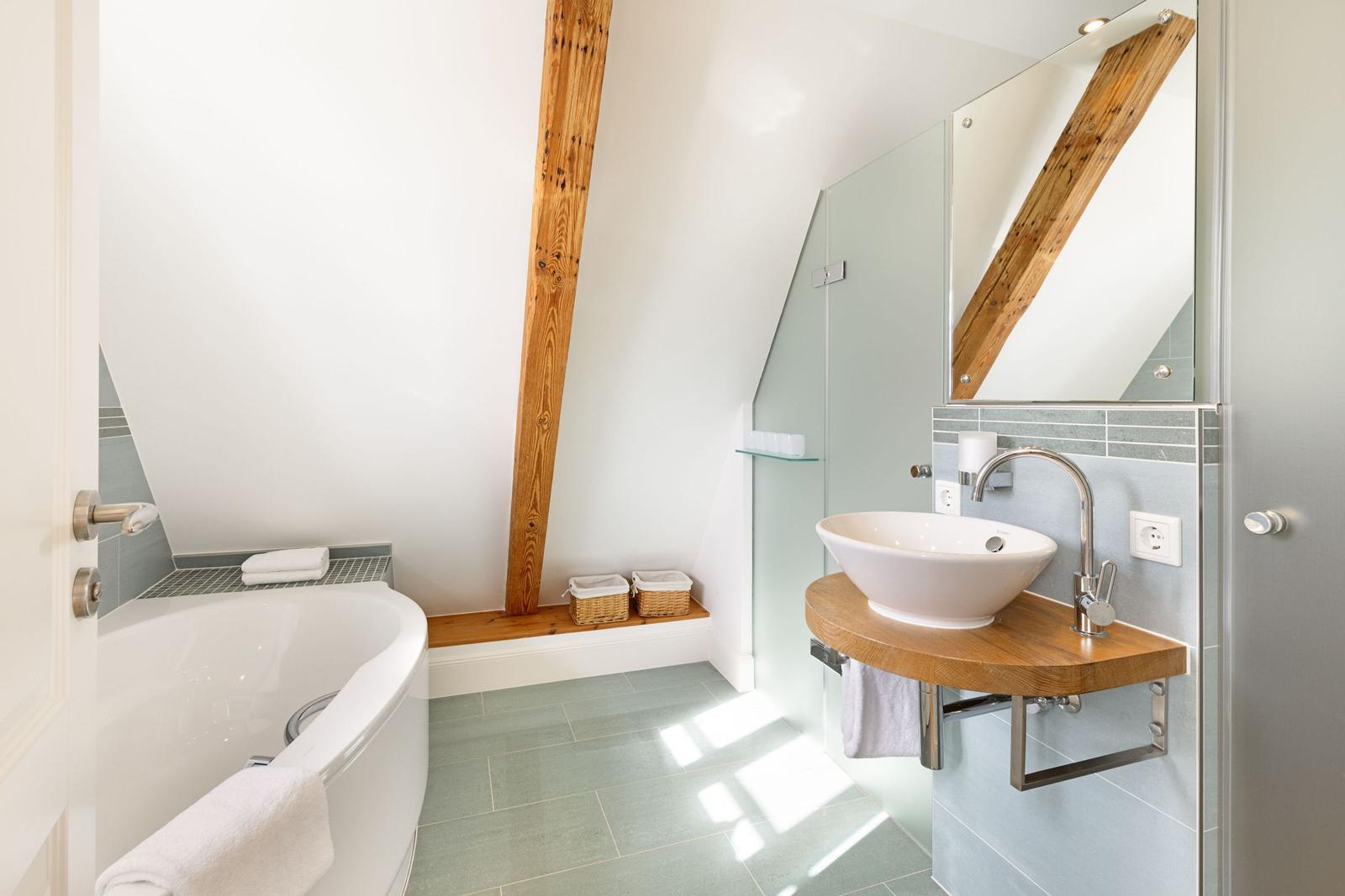 Badezimmer mit Badewanne, Waschbecken und Dusche. Holzbalken und Fliesen sichtbar.