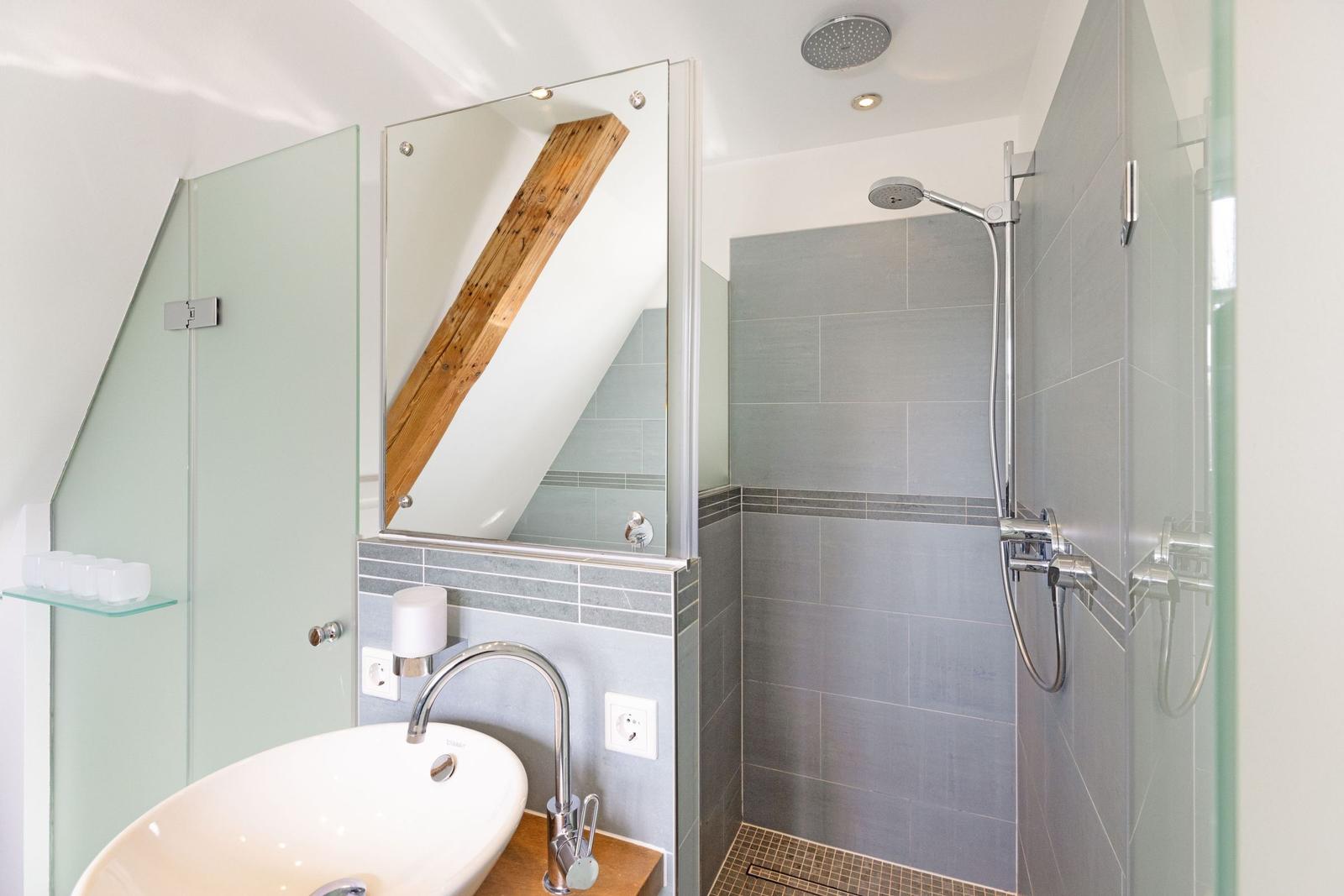 Badezimmer mit Dusche, Waschbecken und Spiegel. Holzbalken sichtbar.