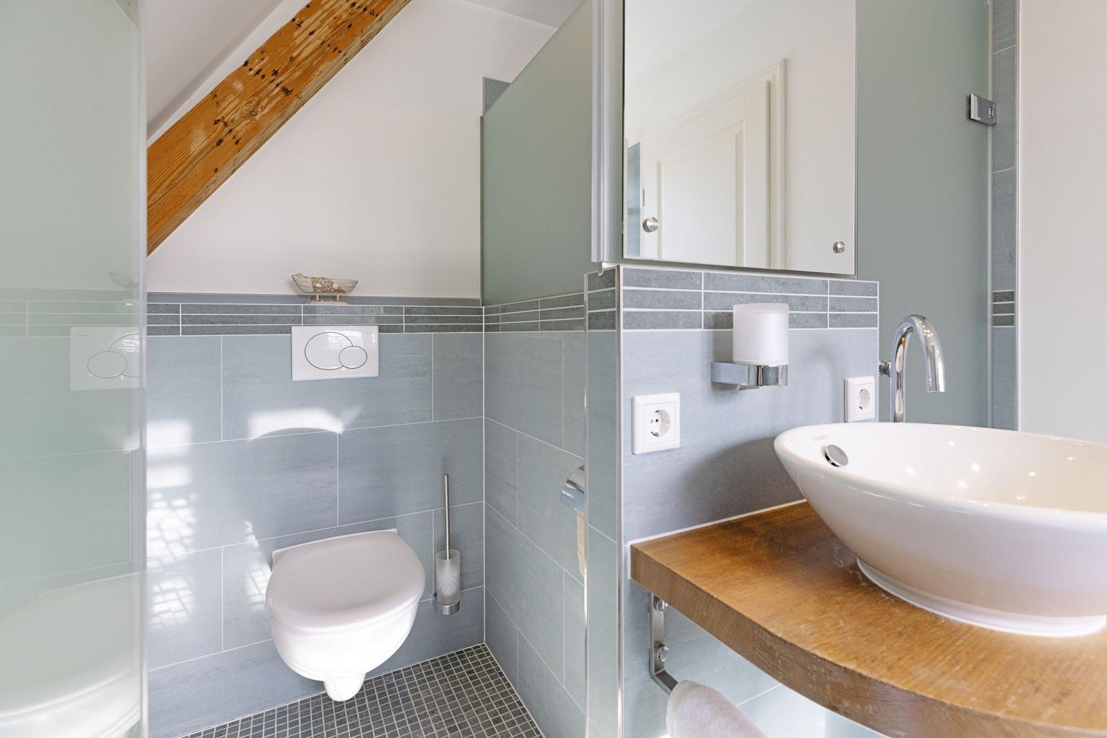 Badezimmer mit Toilette, Waschbecken und Dusche unter Holzbalken.