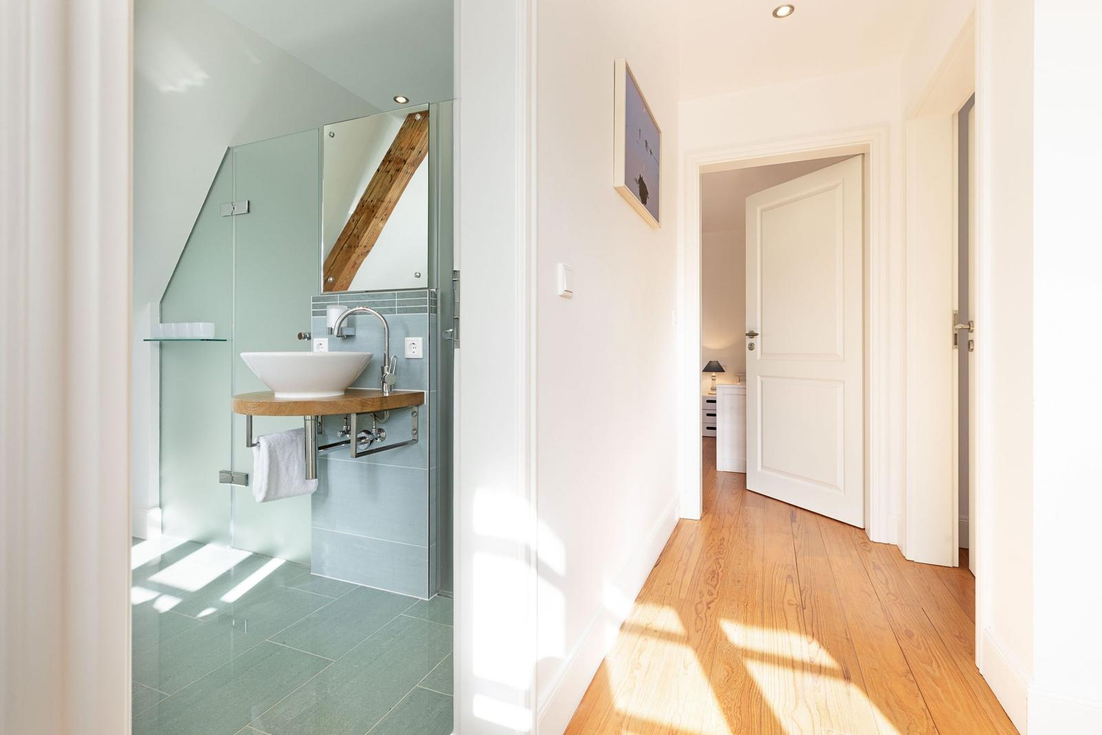 Flur mit Holzboden und Blick in Badezimmer mit Waschbecken und Spiegel.