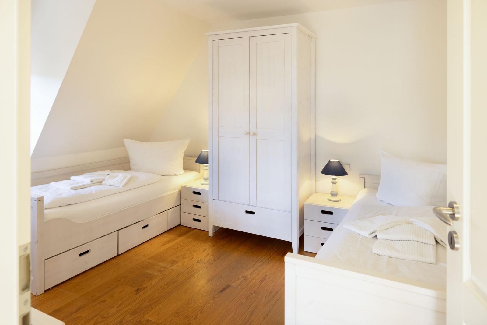 Zimmer mit zwei Betten, Kleiderschrank und Nachttischen mit Lampen.