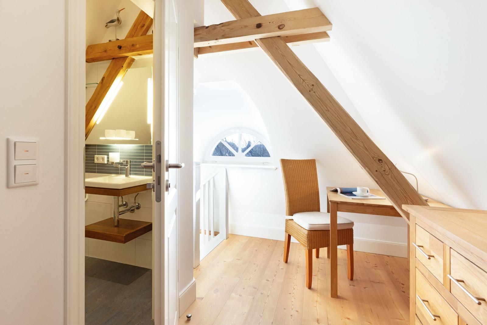 Schlafzimmer mit Schreibtisch, Stuhl und Holzboden. Nebenraum mit Waschbecken und Spiegel.