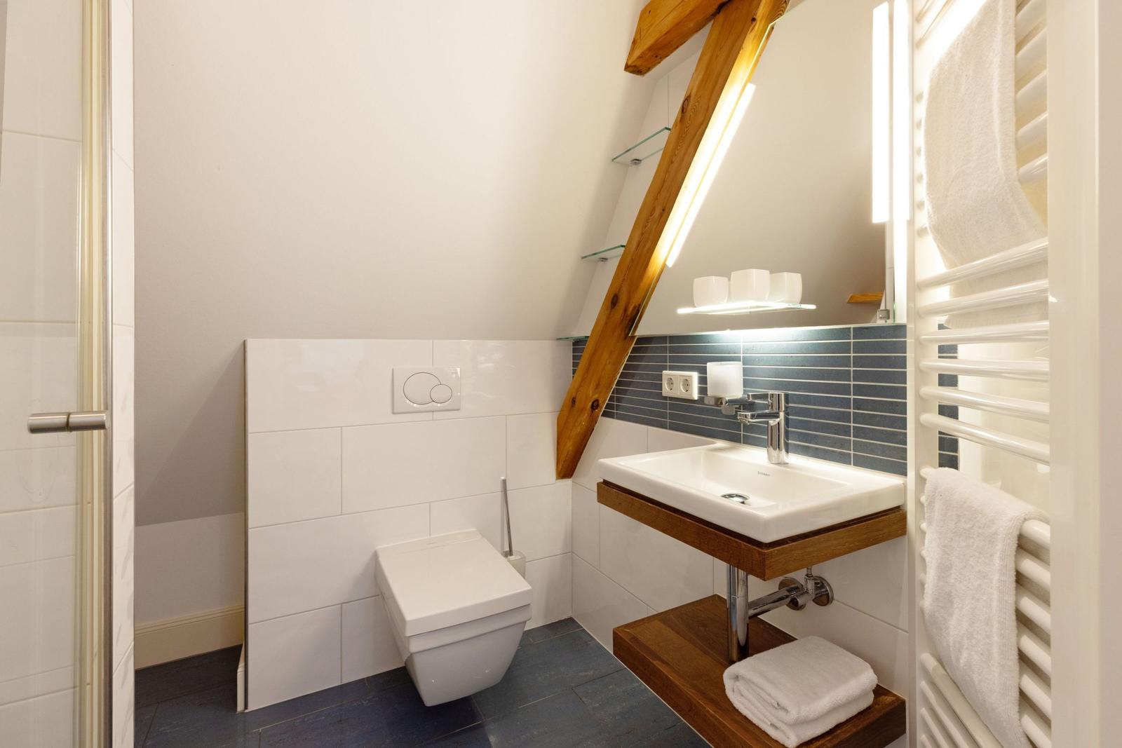 Badezimmer mit Toilette, Waschbecken und Heizkörper. Holzkonstruktion und Fliesen.
