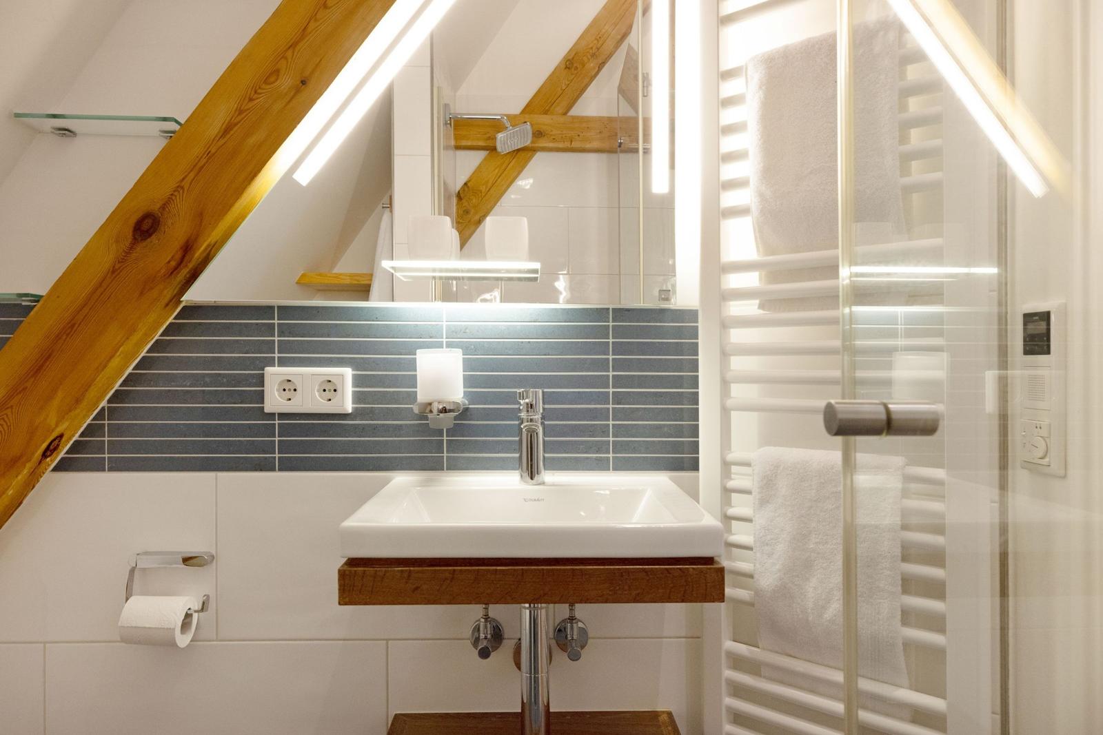 Badezimmer mit Waschbecken, Spiegel und Dusche unter Holzbalken
