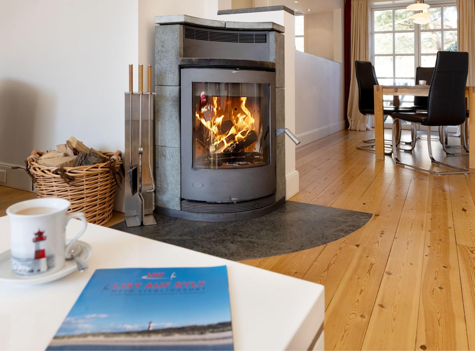 Kamin mit brennendem Holz, Holzboden und Essbereich im Hintergrund.