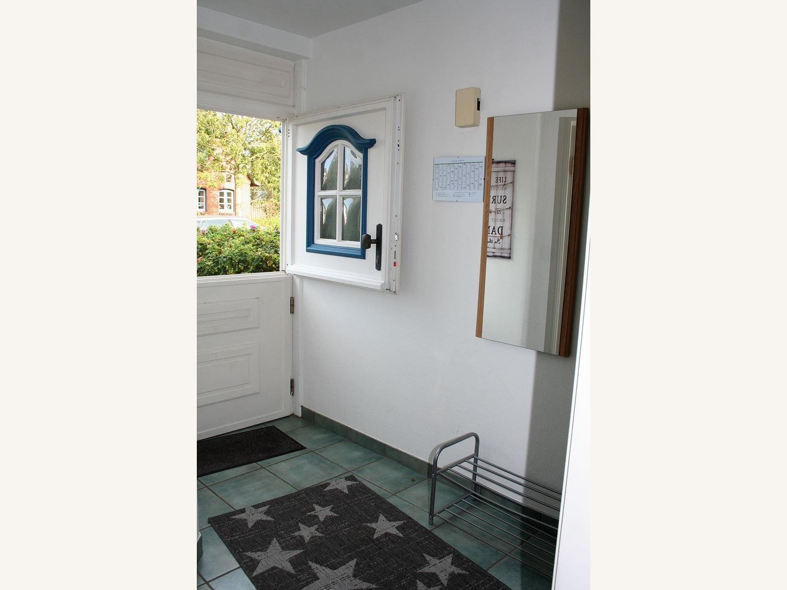 Eingangsbereich mit Tür, Fenster und Teppich. Wandspiegel und Kalender sind angebracht.