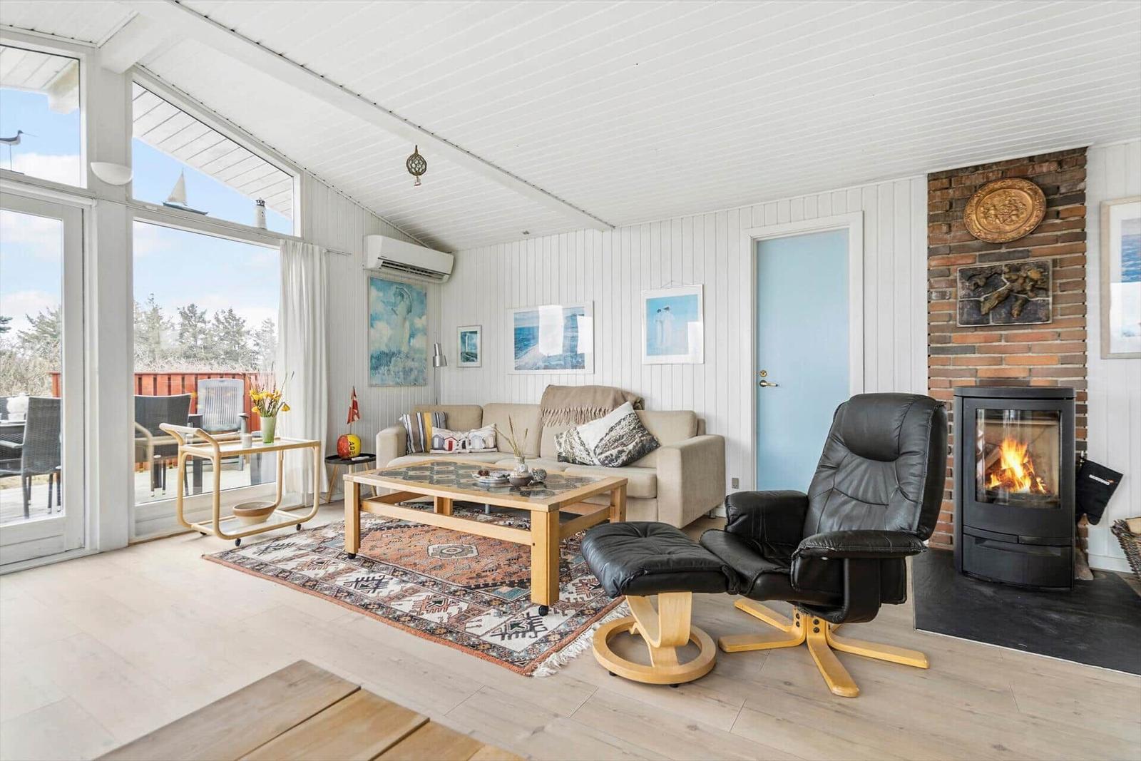 Wohnzimmer mit Sofa, Sessel und Kamin. Große Fenster und Holzboden.