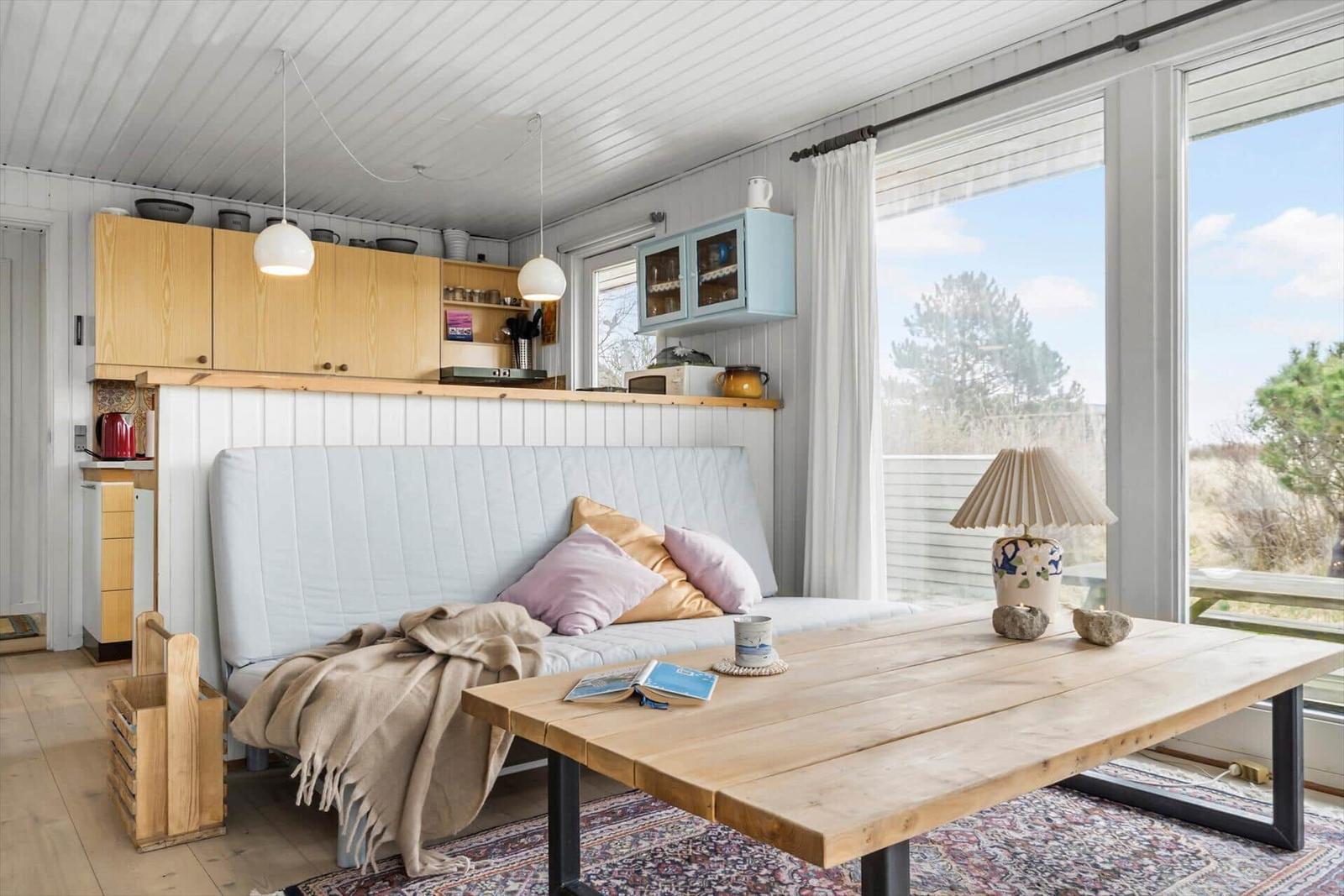 Ein Raum mit Sofa, Holztisch und großen Fenstern. Küche mit Holzschränken und blauem Schrank.