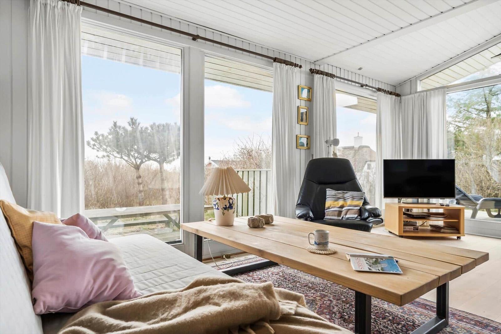 Ein Wohnzimmer mit großem Fenster, Couch, Tisch und Fernseher.