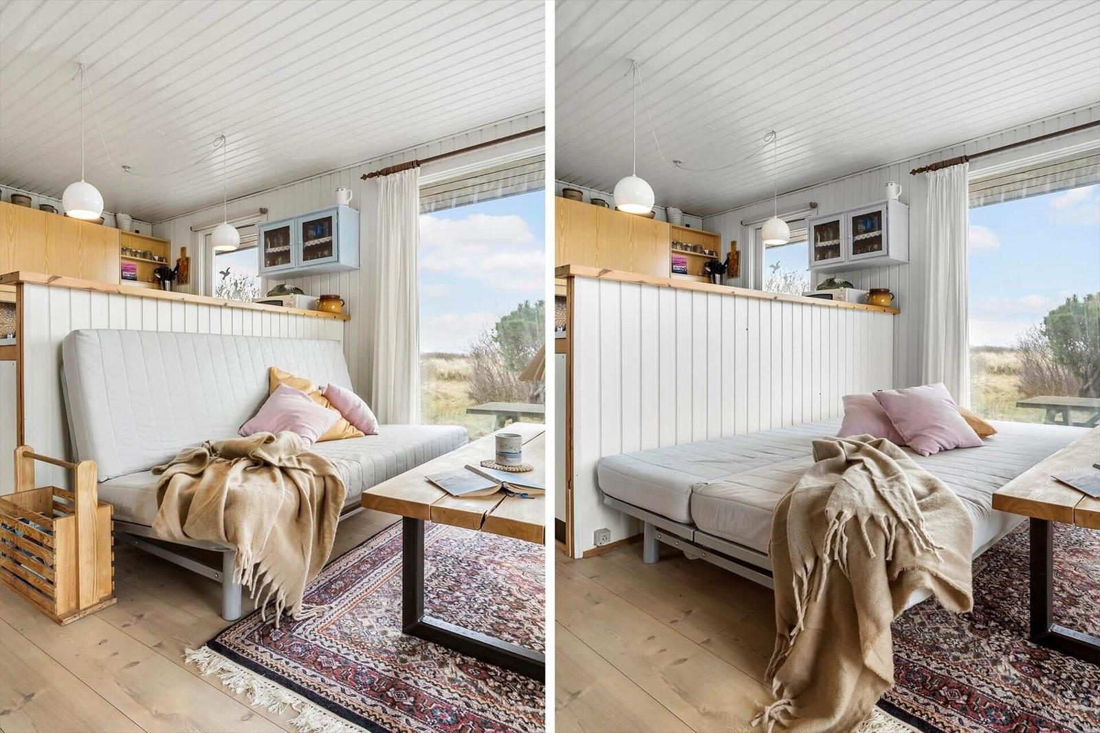 Zimmer mit Schlafcouch, Holztisch und Blick auf die Landschaft.