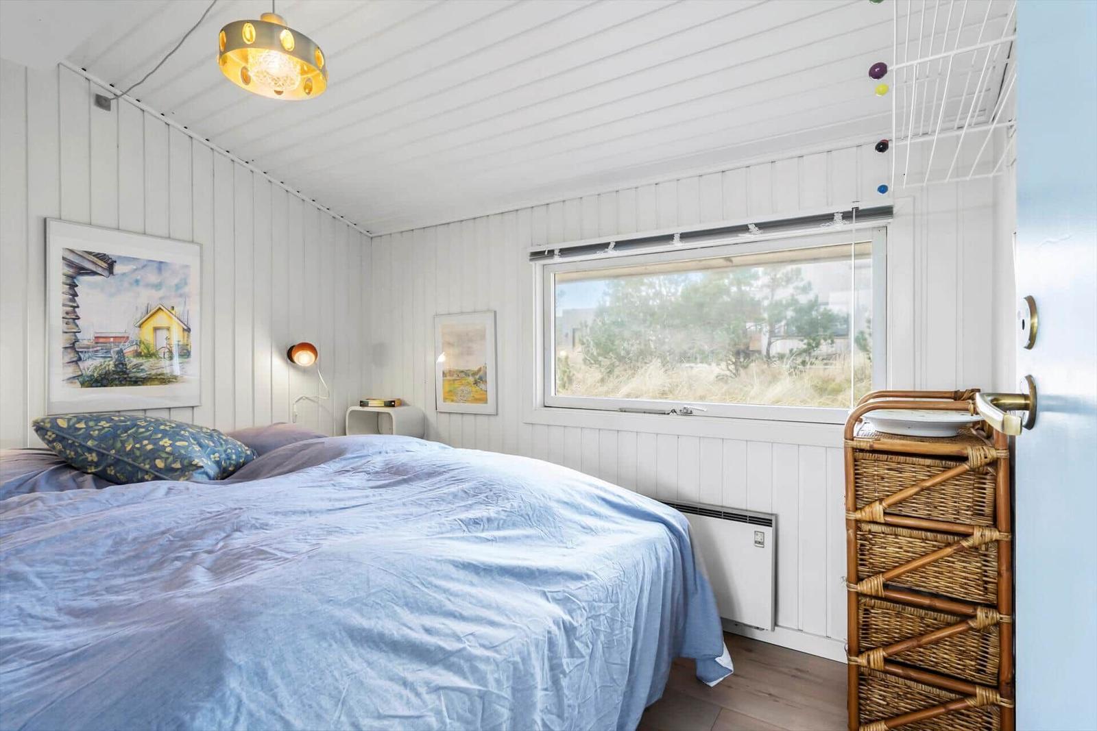 Schlafzimmer mit Bett, Fenster und Wandbildern. Decke mit Lampe und Körbchenregal.